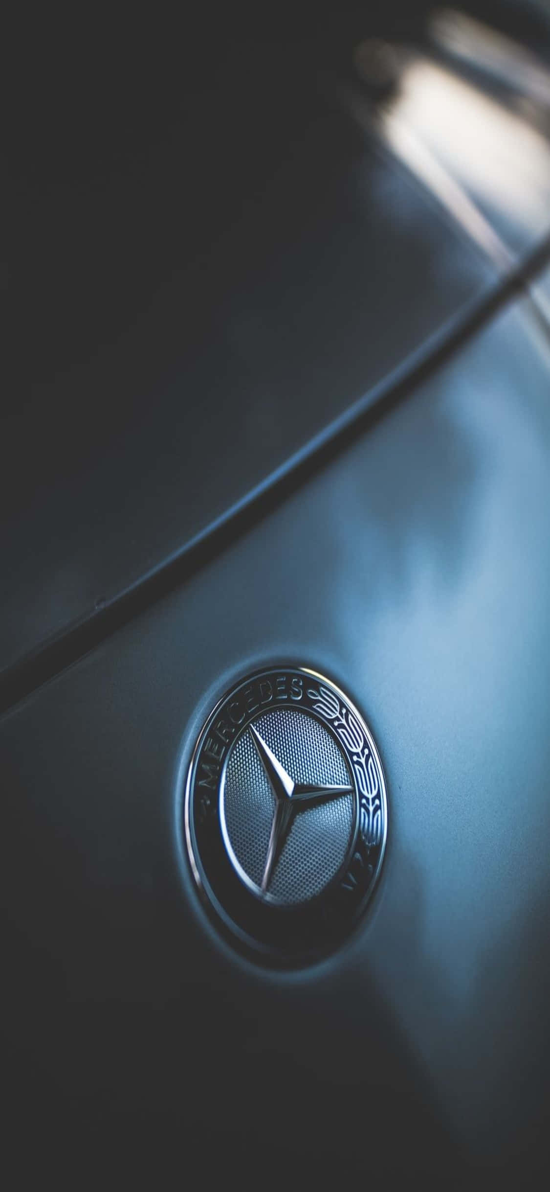 Mercedes 桌布 壁紙 — 賓士標誌在柔和的藍光下於流線型引擎蓋上閃爍的特寫。