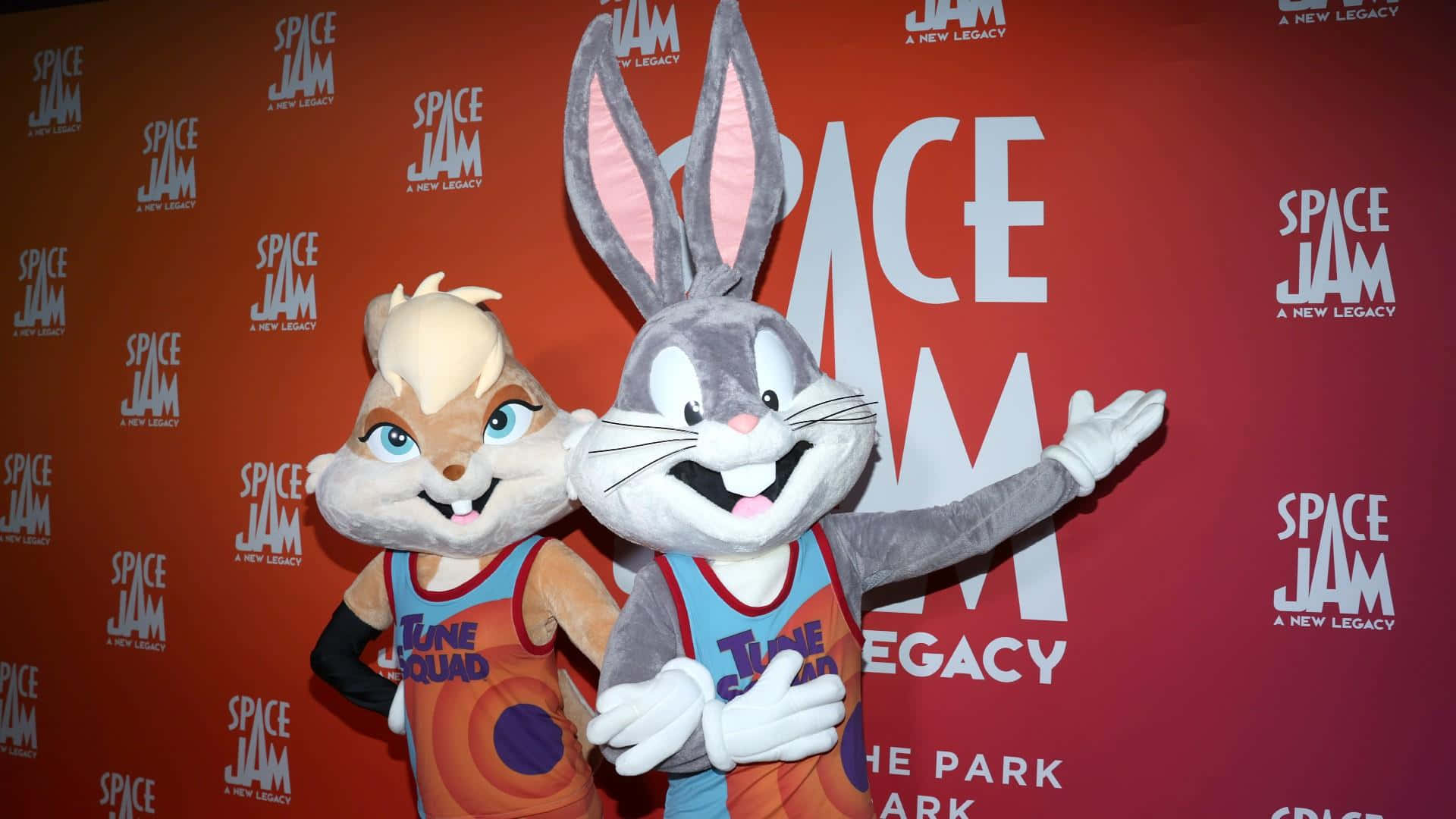 Space Jam A New Legacy 桌布 壁紙 — 賓尼兔和蘿拉兔穿著Tune Squad球衣，在紅色Space Jam背景前愉快地擺姿勢。