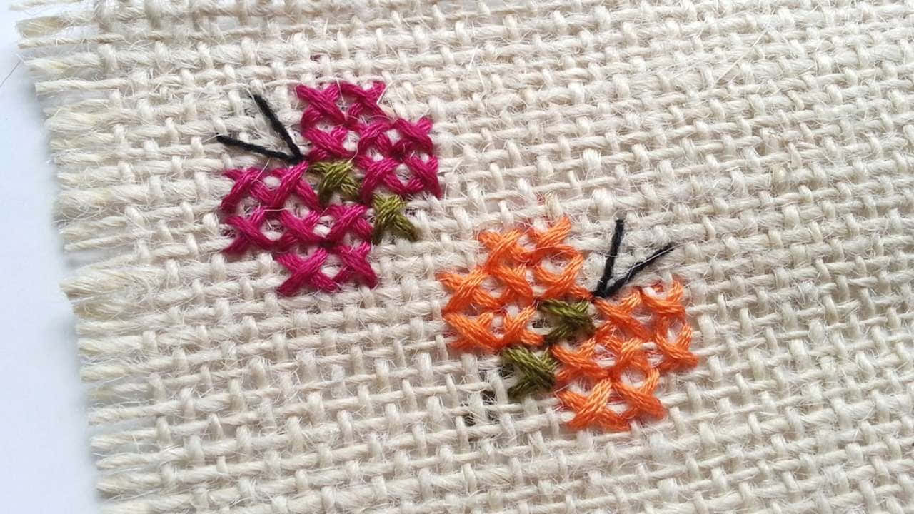 Butterfly Stitch 桌布 壁紙 — 質感米白色布料上鮮豔粉紅與橙色十字繡花朵、綠葉與黑色花莖的特寫。