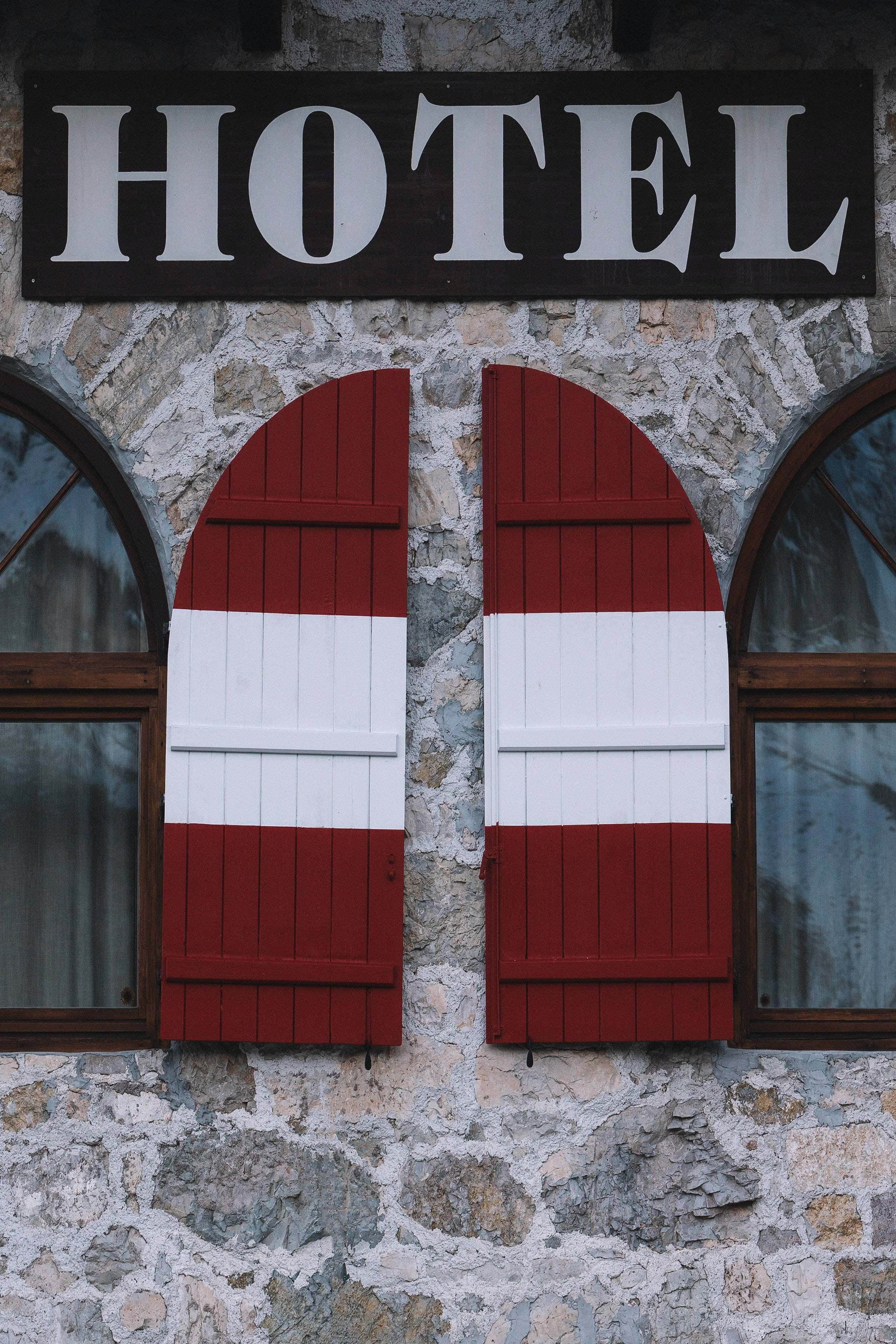 Hotel 桌布 壁紙 — 質樸的石頭飯店外牆，在醒目的黑色招牌（白色字體）下方，設有拱形紅色和白色百葉窗。