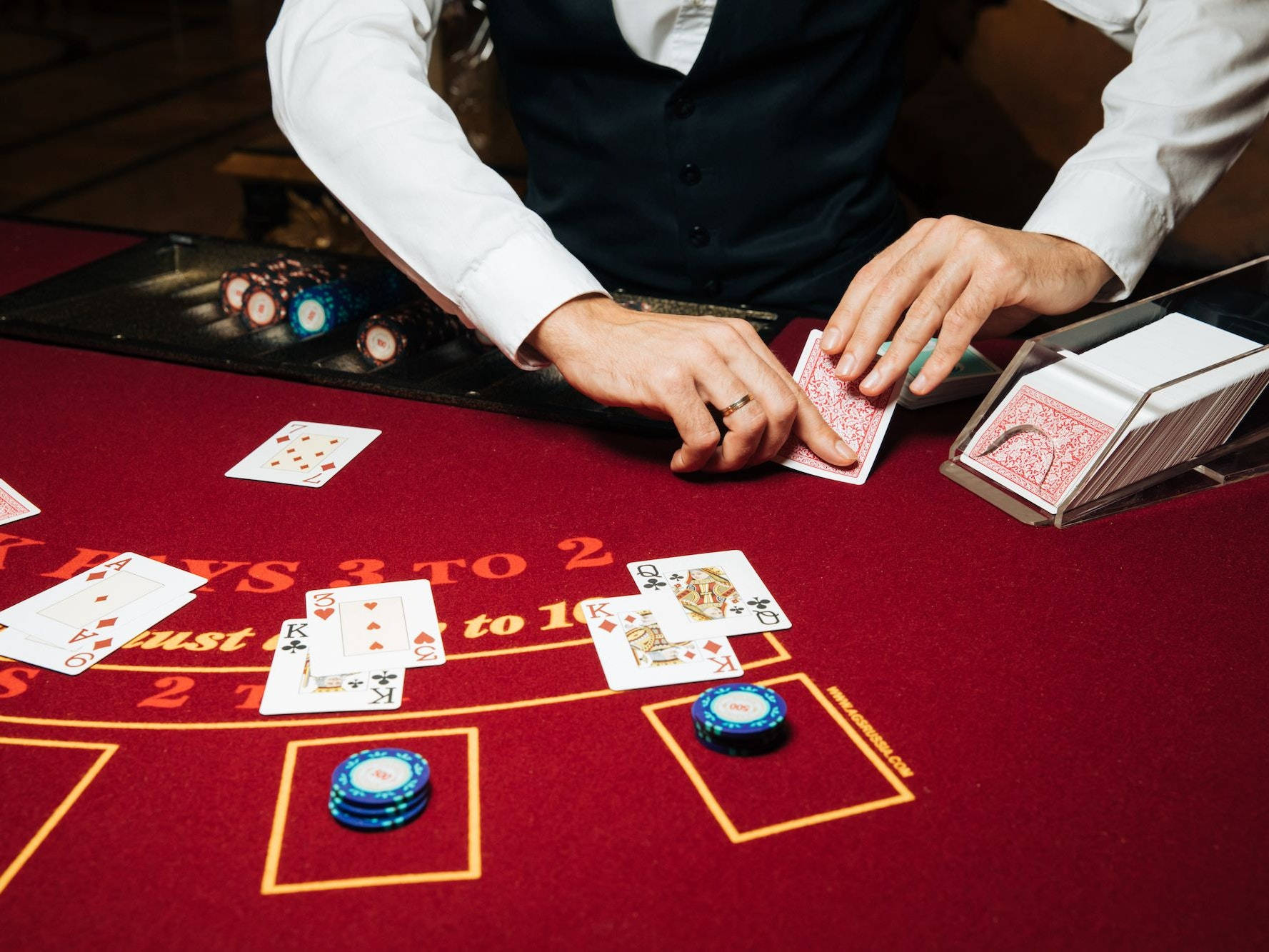 Casino 桌布 壁紙 — 賭場荷官在紅色絨布桌上洗牌，桌上有藍色籌碼和翻開的撲克牌。