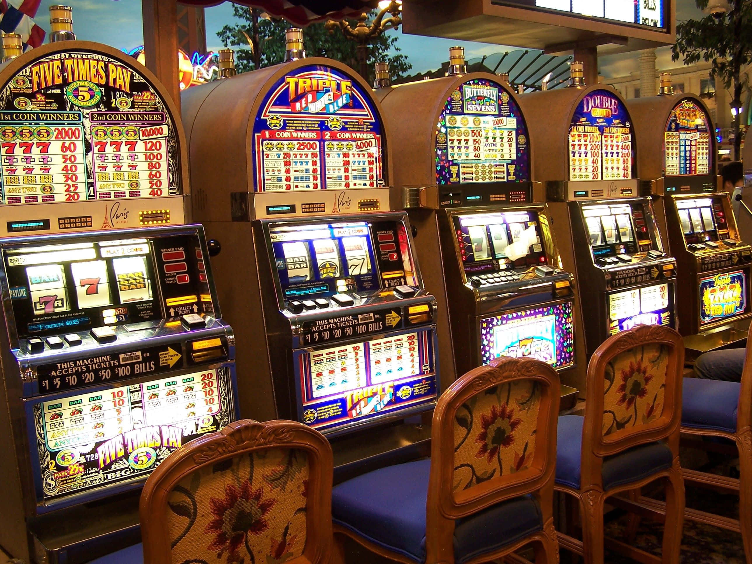 Slot Machine 桌布 壁紙 — 賭場遊戲區內一排燈光明亮的復古老虎機，配有華麗花卉圖案椅子。