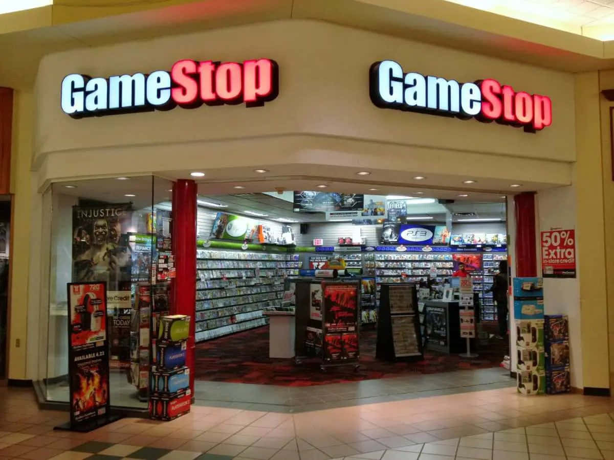 GameStop 桌布 壁紙 — 購物中心內一間GameStop店鋪入口，光線明亮，有紅色柱子和擺滿電子遊戲及主機的貨架。