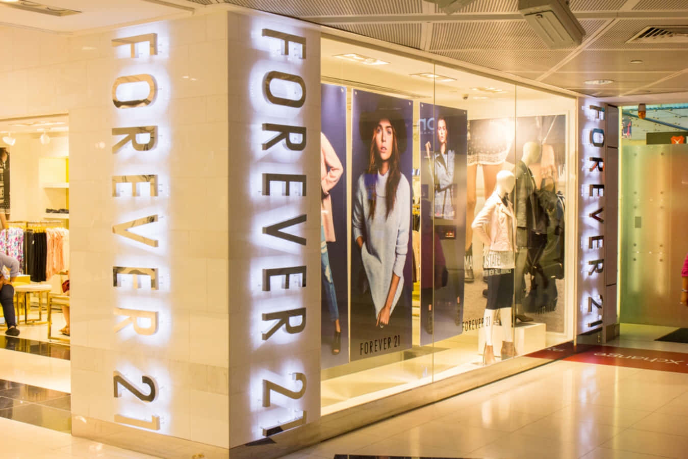 永遠21 桌布 壁紙 — 購物中心內明亮照明的Forever 21店鋪正面，配有發光標誌和展示時尚服裝的人體模型。