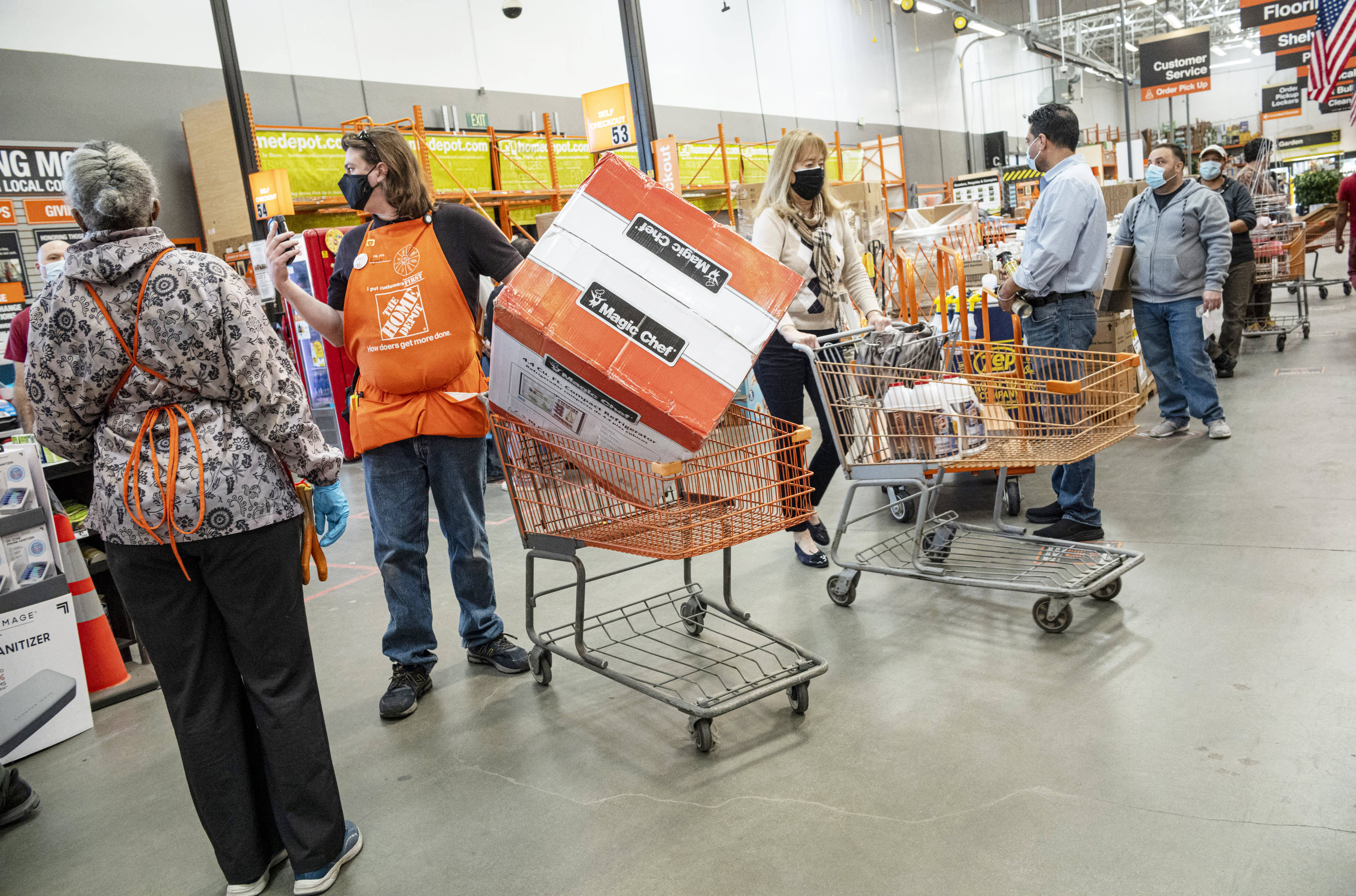 Home Depot 桌布 壁紙 — 購物者和員工在繁忙的Home Depot通道中穿梭，手推車上堆滿大型盒裝物品並戴著安全口罩。