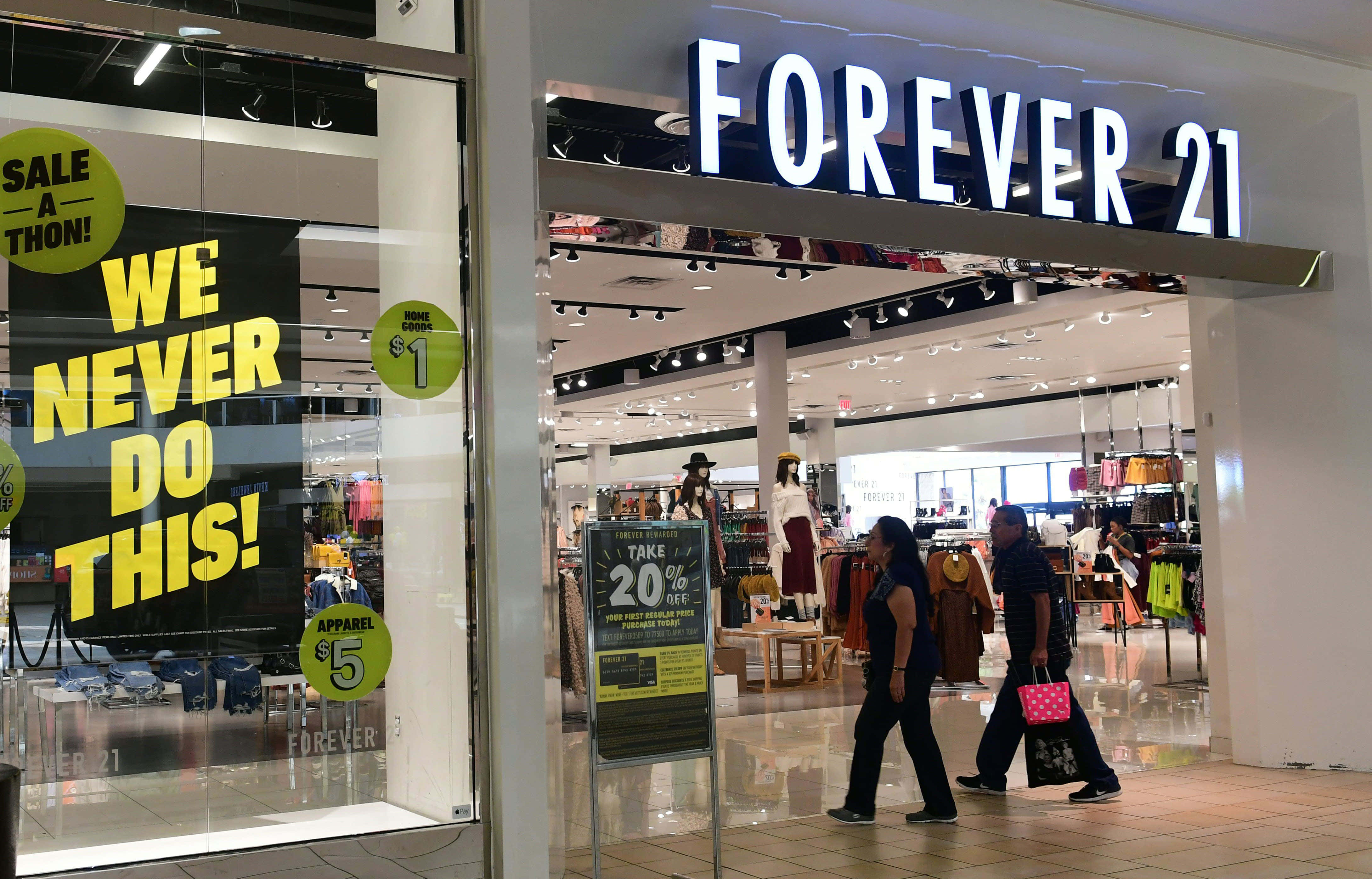 永遠21 桌布 壁紙 — 購物者走過一間Forever 21商店，店內有醒目的特價標誌和明亮的室內燈光。