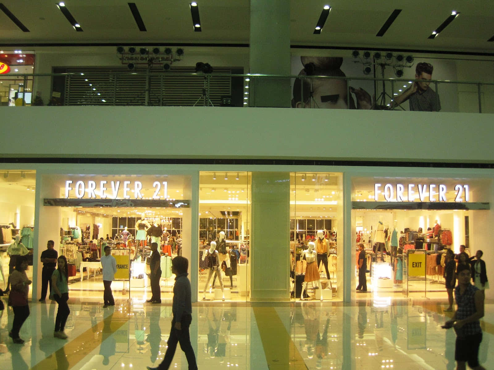 永遠21 桌布 壁紙 — 購物者走過光線明亮的Forever 21商店，位於一個繁忙的兩層購物中心，地板反射光線，頭頂有燈光。
