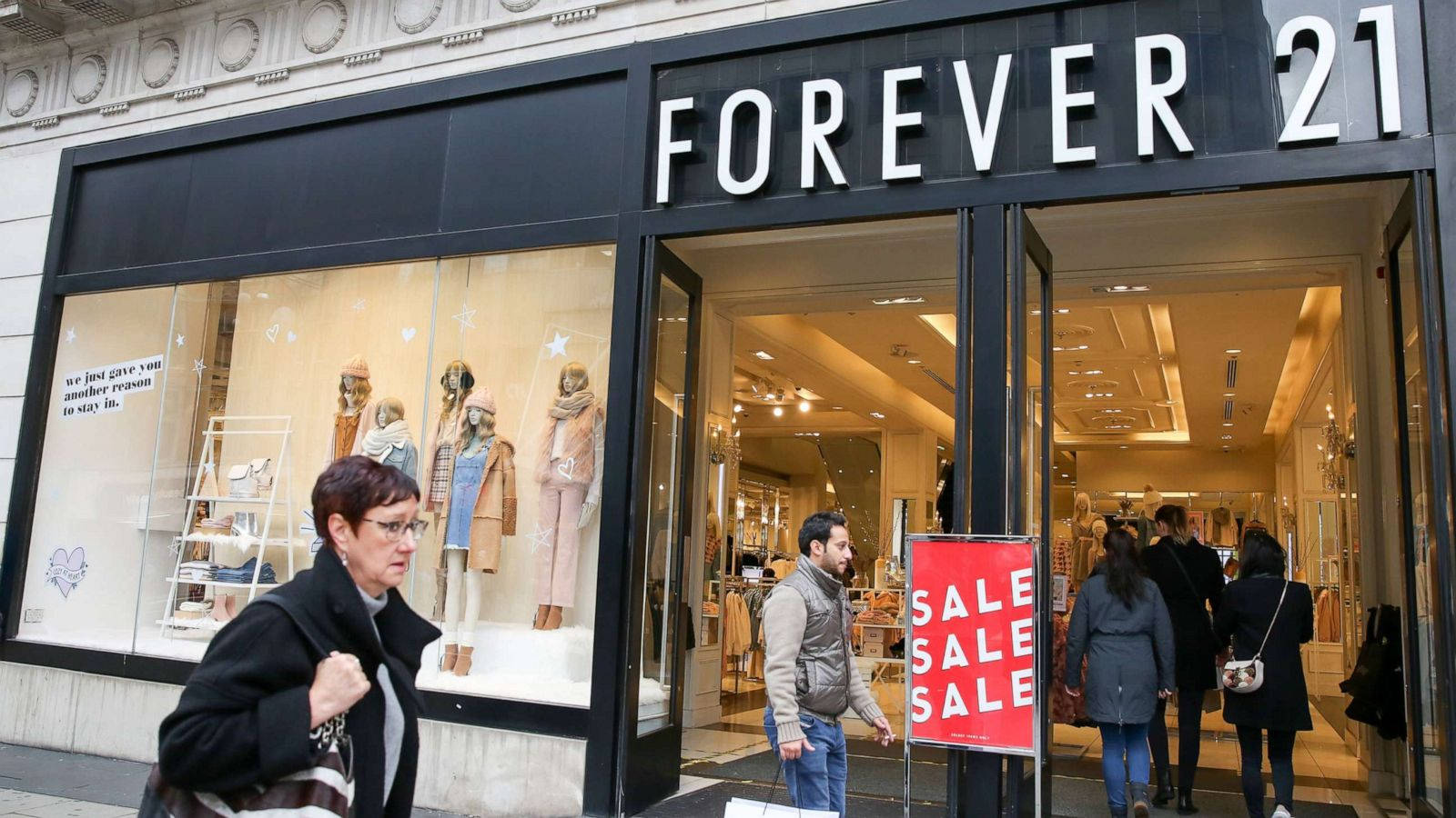 永遠21 桌布 壁紙 — 購物者進出一間Forever 21商店，店內有明亮的特價標誌和櫥窗展示的人體模型。