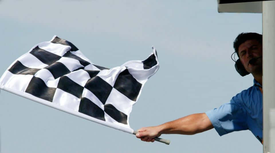 Chequered Flag 桌布 壁紙 — 賽事工作人員在晴朗的天空下揮動方格旗，進行賽車活動。