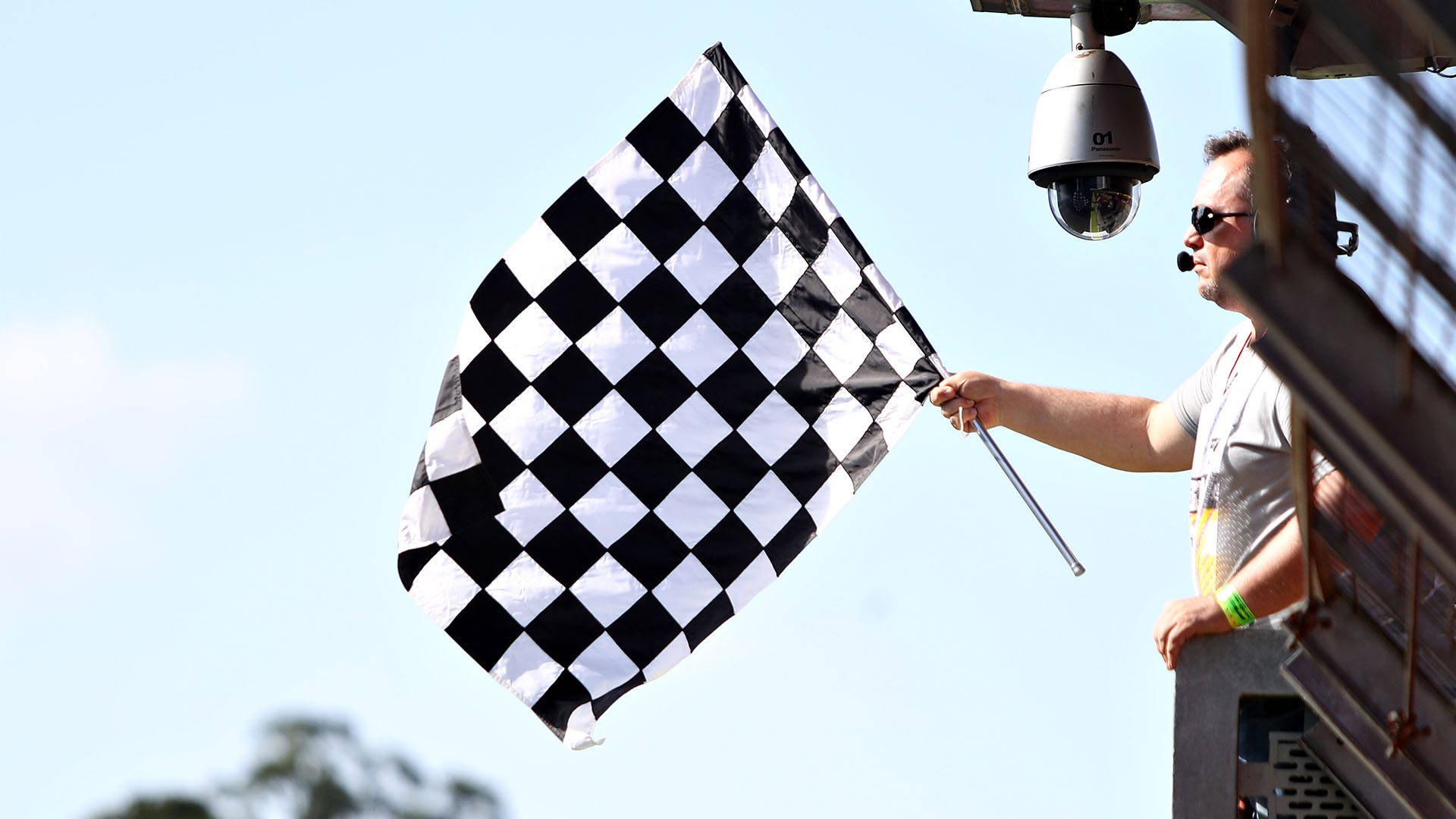 Checkered Flag 桌布 壁紙 — 賽事工作人員在賽車活動中，於晴朗藍天下揮動方格旗。