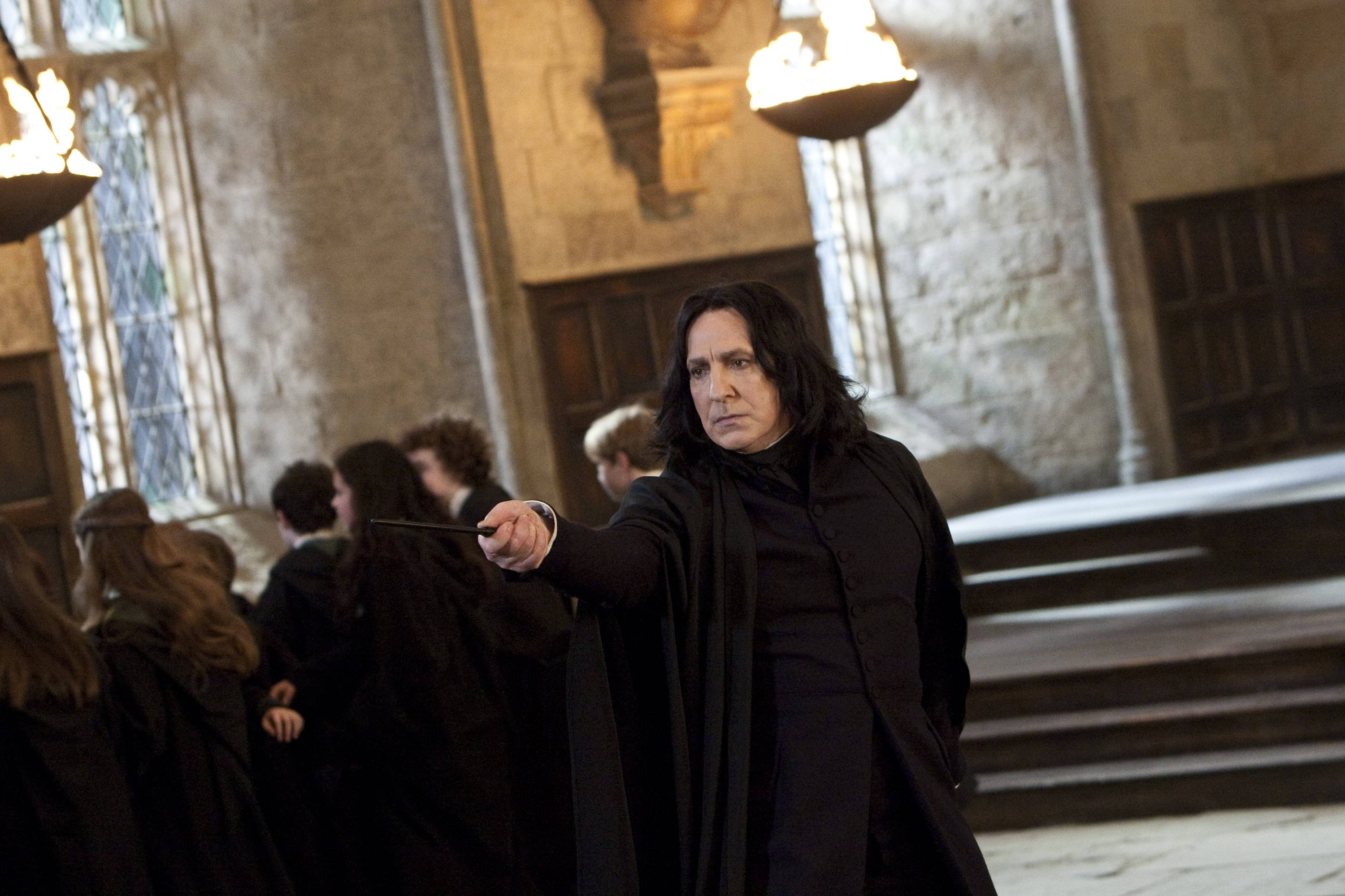Severus Snape 桌布 壁紙 — 賽佛勒斯·石內卜在霍格華茲大禮堂中，在搖曳的火炬光芒下，表情嚴肅地舉起魔杖。