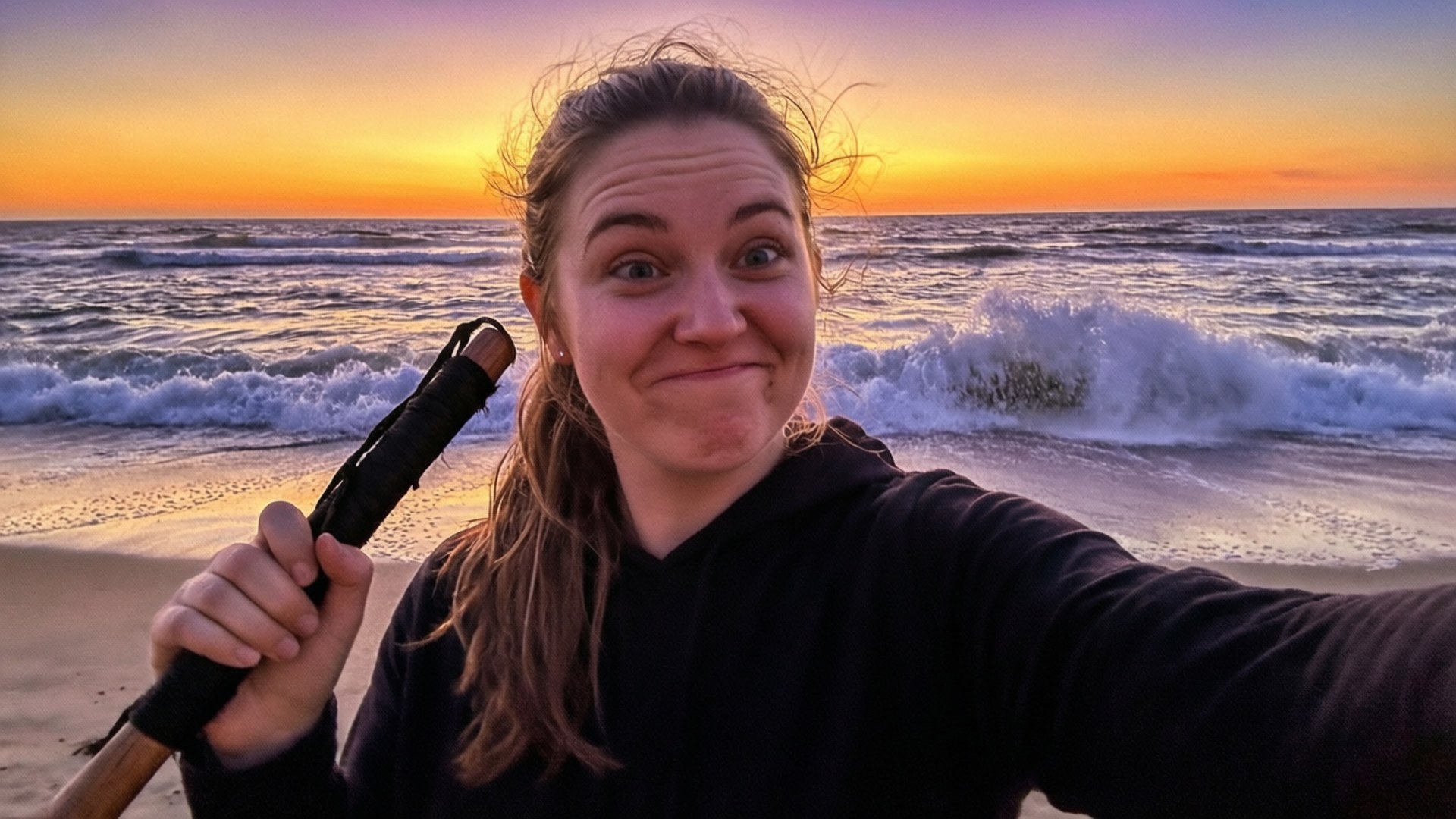賽爾菲的海灘樂趣 壁紙 — 一個帶有頑皮笑容的女人在海灘日落時分拿著槳自拍。