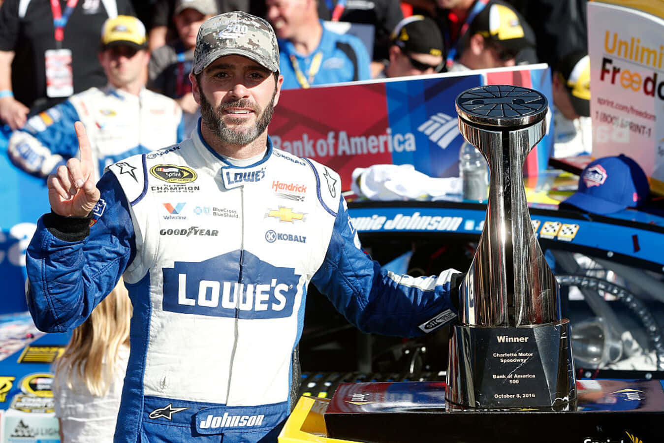 Jimmie Johnson 桌布 壁紙 — 賽車手 Jamie Johnson 在夏洛特賽車場陽光普照的一天，手持閃閃發光的獎盃慶祝勝利。