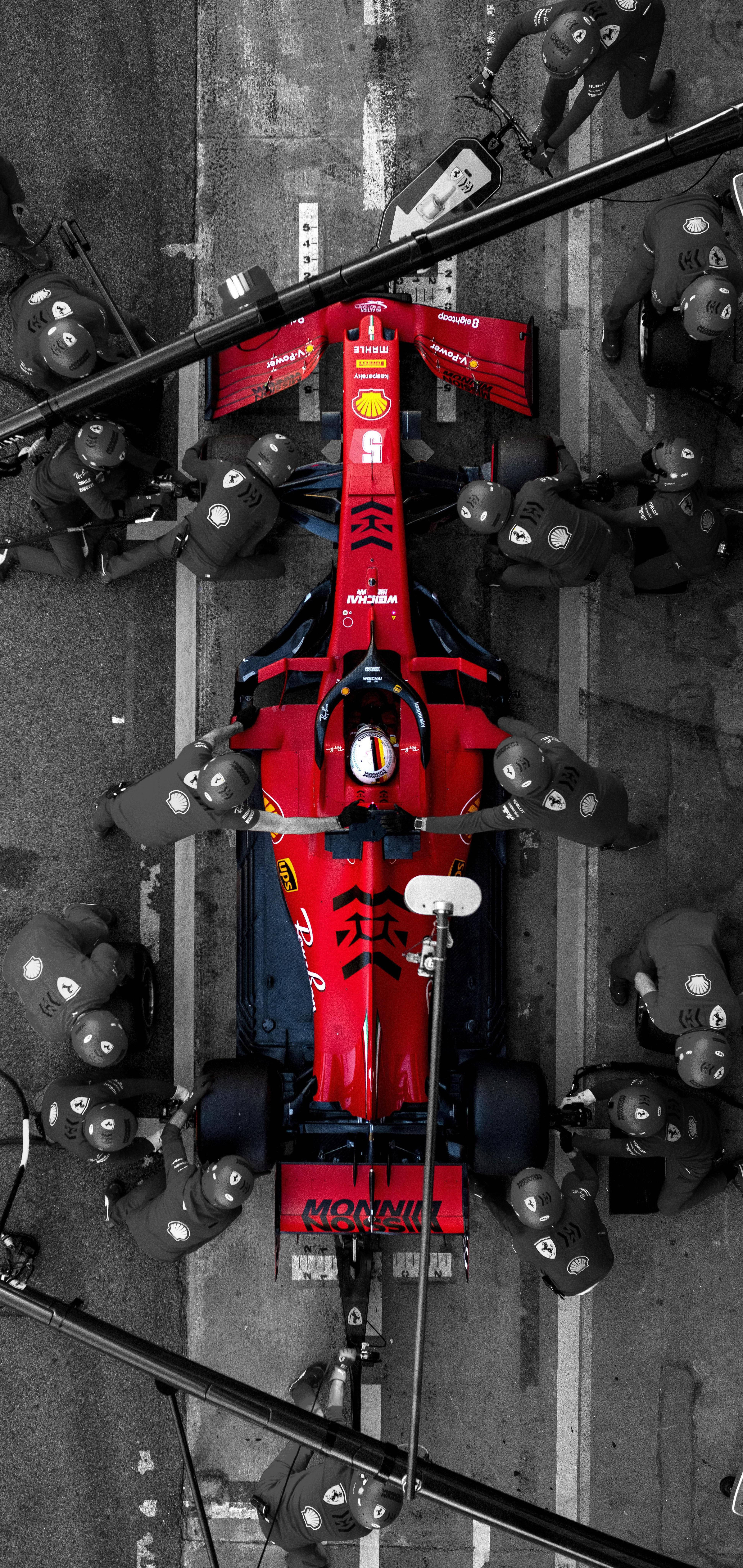 F1 iPhone 壁紙 桌布 壁紙 — 賽道上維修站中，一輛紅色一級方程式賽車被機械師包圍的鳥瞰圖。