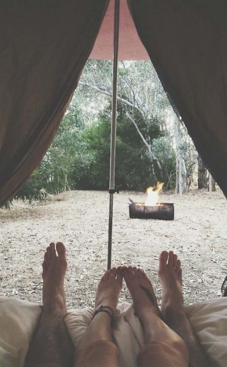 Minimalist Camping 桌布 壁紙 — 赤腳在帳篷內休息，望著樹林空地中燃燒的營火。