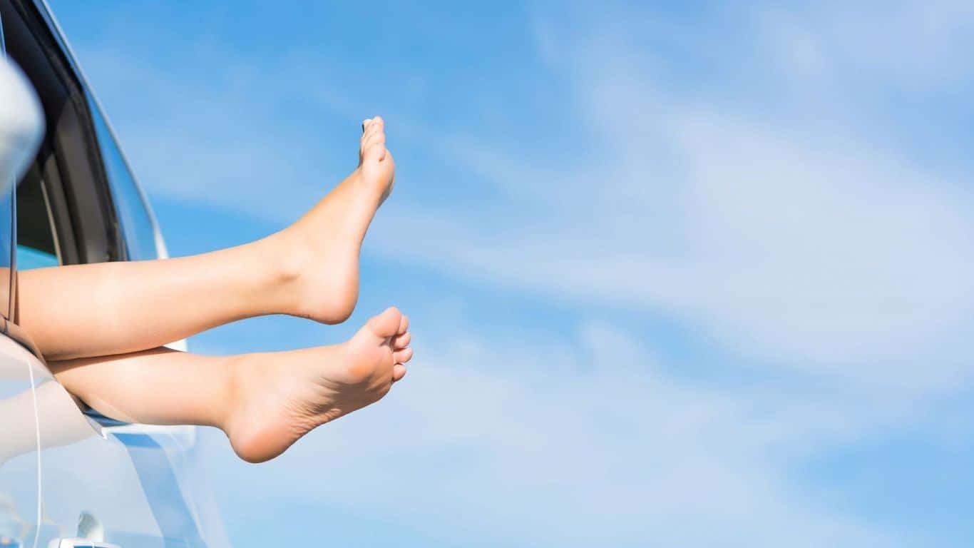 feet 桌布 壁紙 — 赤腳從車窗伸出，懸掛在明亮藍天與縷縷白雲的背景中。