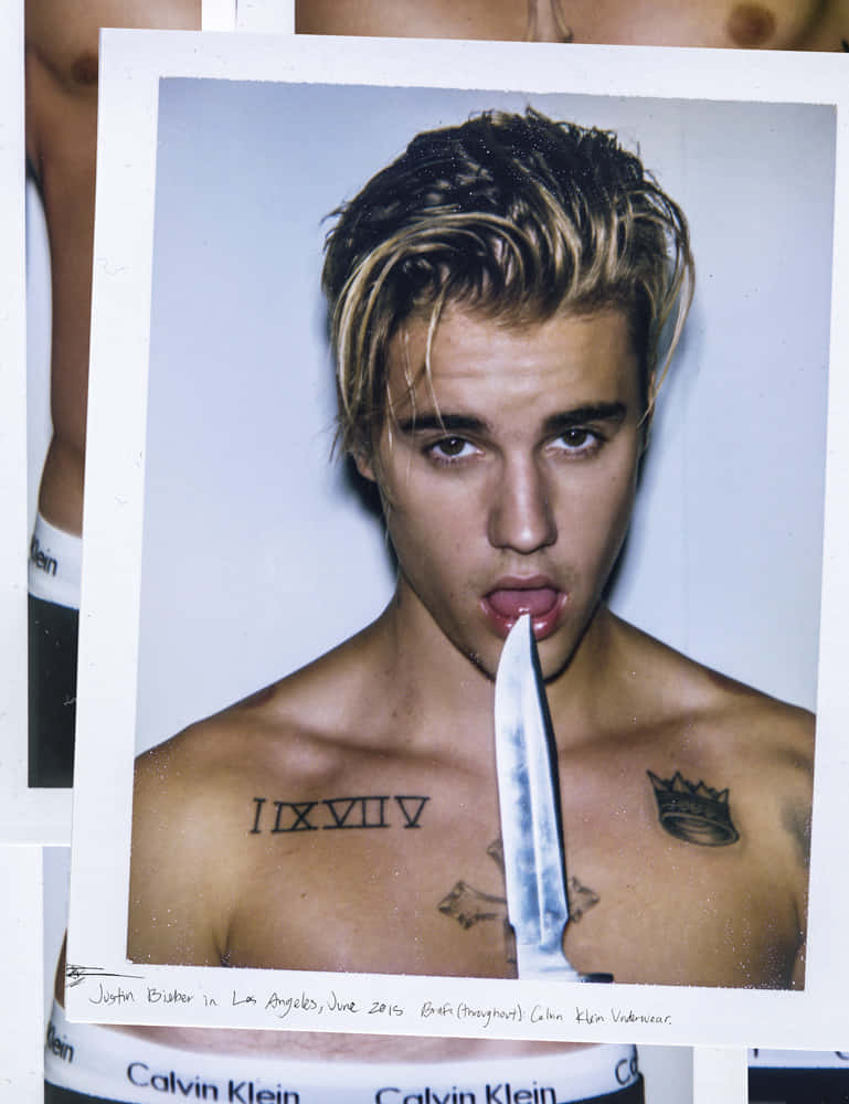 Justin Bieber 2015 桌布 壁紙 — 赤裸上身的Justin Bieber伸出舌頭，同時將刀放在嘴唇上，照片風格類似拍立得。