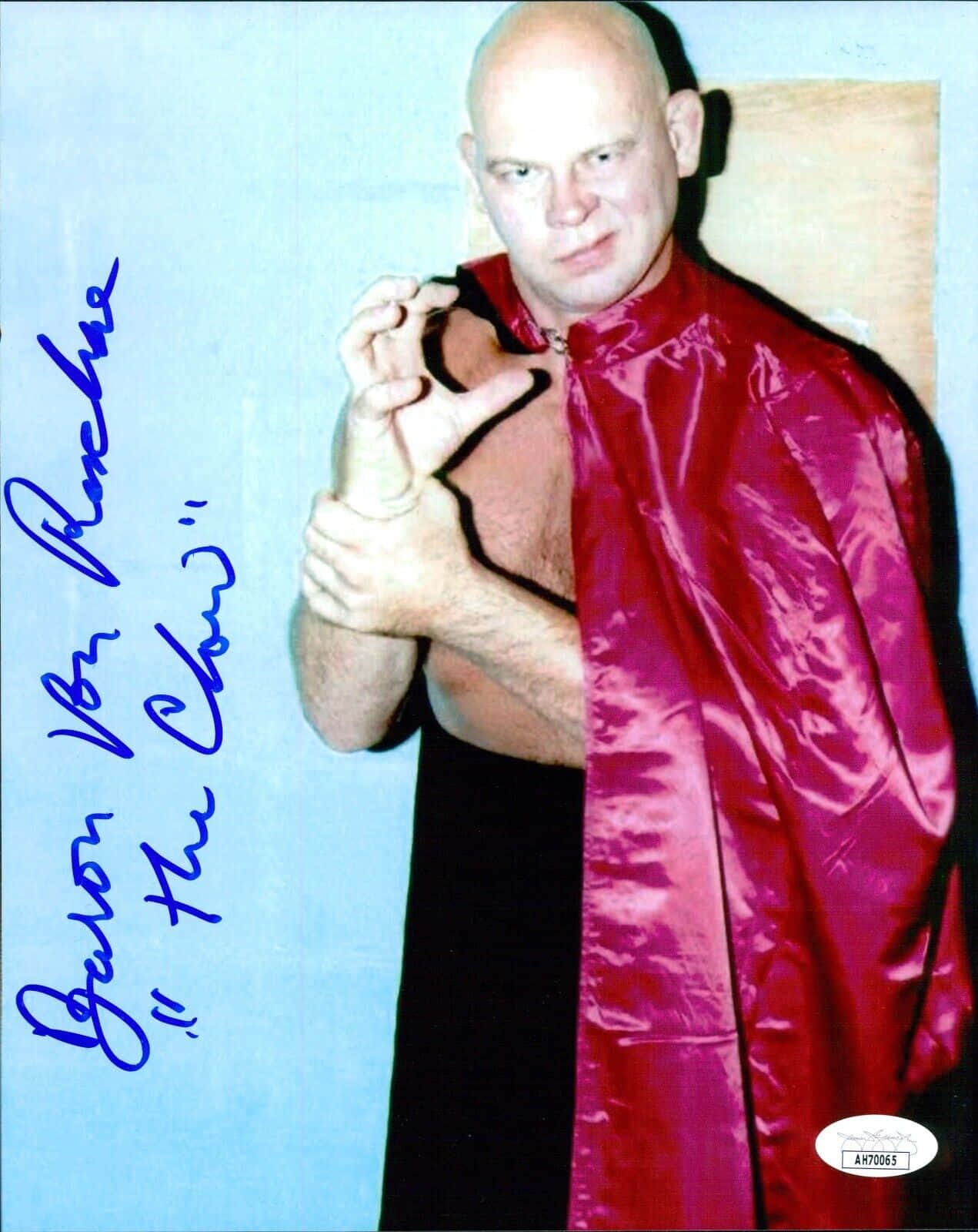 摔角 桌布 壁紙 — 赤裸上身的摔角手 Brutus 'The Barber' Beefcake 穿著閃亮的紅色斗篷，在純藍色牆壁前擺姿勢，露出他的簽名。