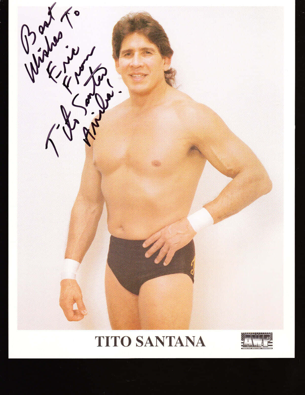 poster 桌布 壁紙 — 赤裸上身的摔角選手 Tito Santana 自信地擺姿勢，身穿黑色三角褲和白色護腕，背景為純白色，並附有他的簽名。