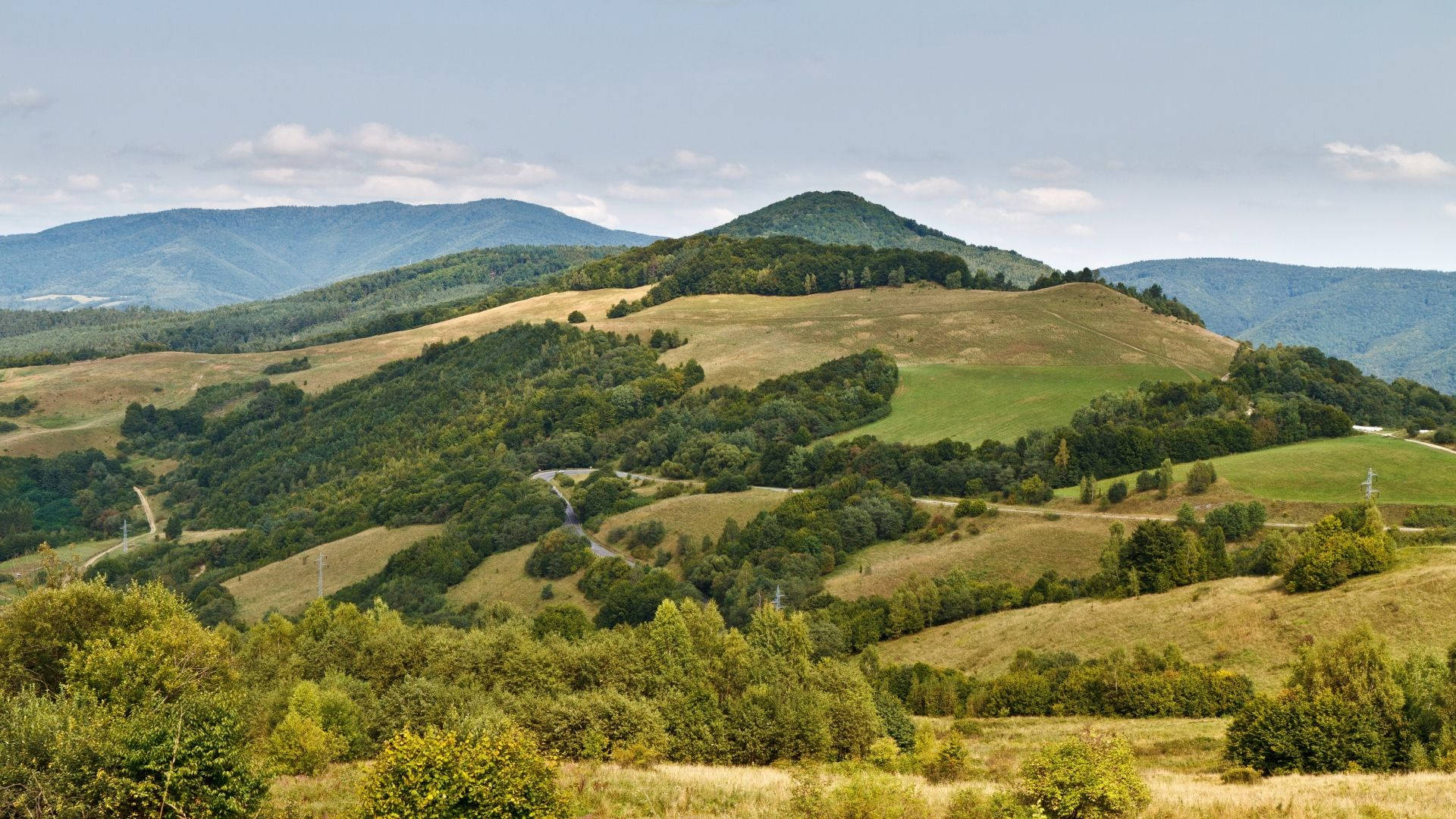 Slovakia 桌布 壁紙 — 起伏的綠色山丘，點綴著樹木和蜿蜒的道路，天空部分多雲。