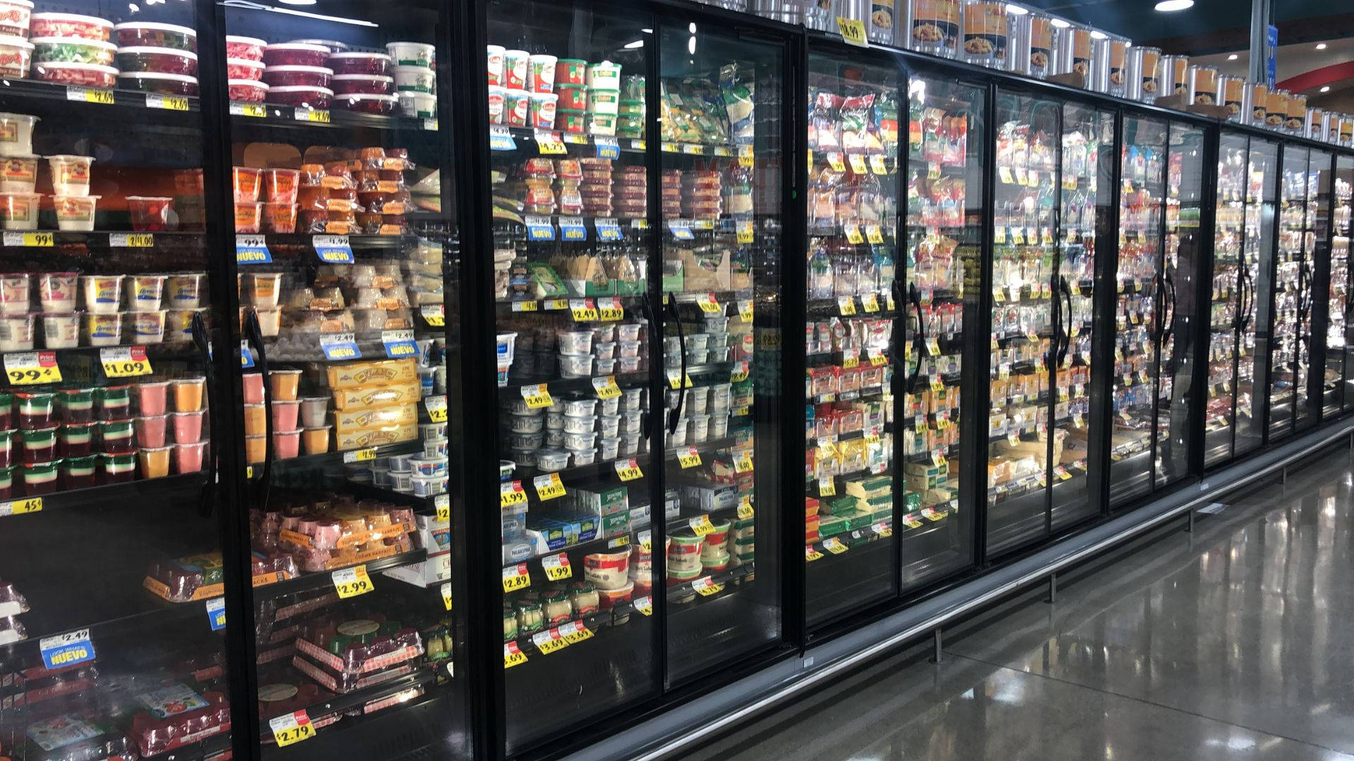 Market 桌布 壁紙 — 超市內一排長長的玻璃門冷凍櫃，在明亮的螢光燈下裝滿了色彩繽紛的包裝冷凍食品。