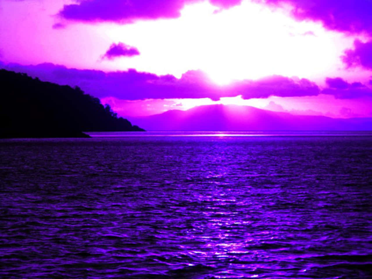 Blue And Purple Sunset 桌布 壁紙 — 超現實的紫色日落，平靜的海面上有遠山和發光雲層下的陸地剪影。