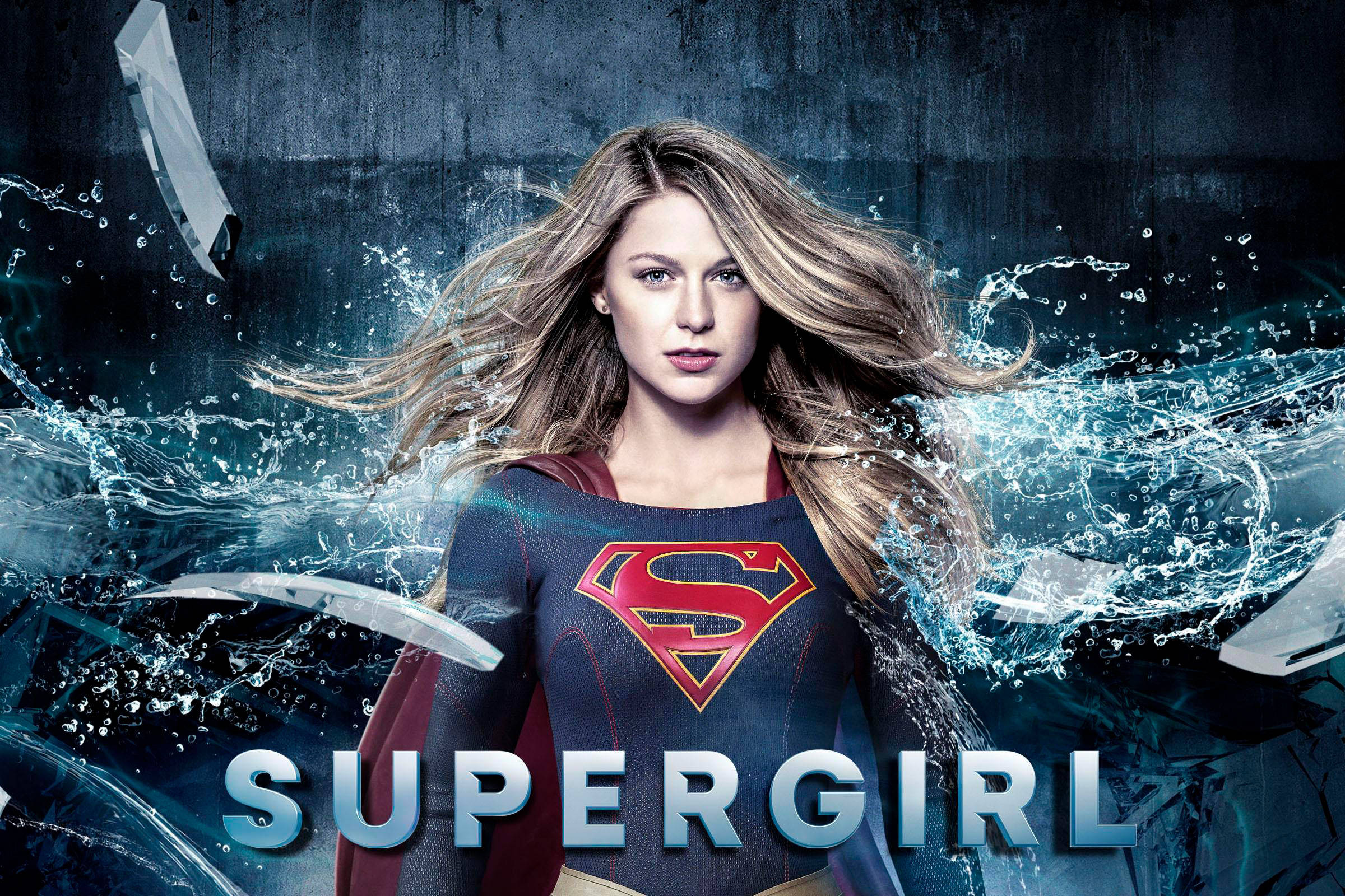 Supergirl 桌布 壁紙 — 超級女孩強勢站立，水和破碎的玻璃在她周圍爆炸，形成一個動態的超級英雄場景。