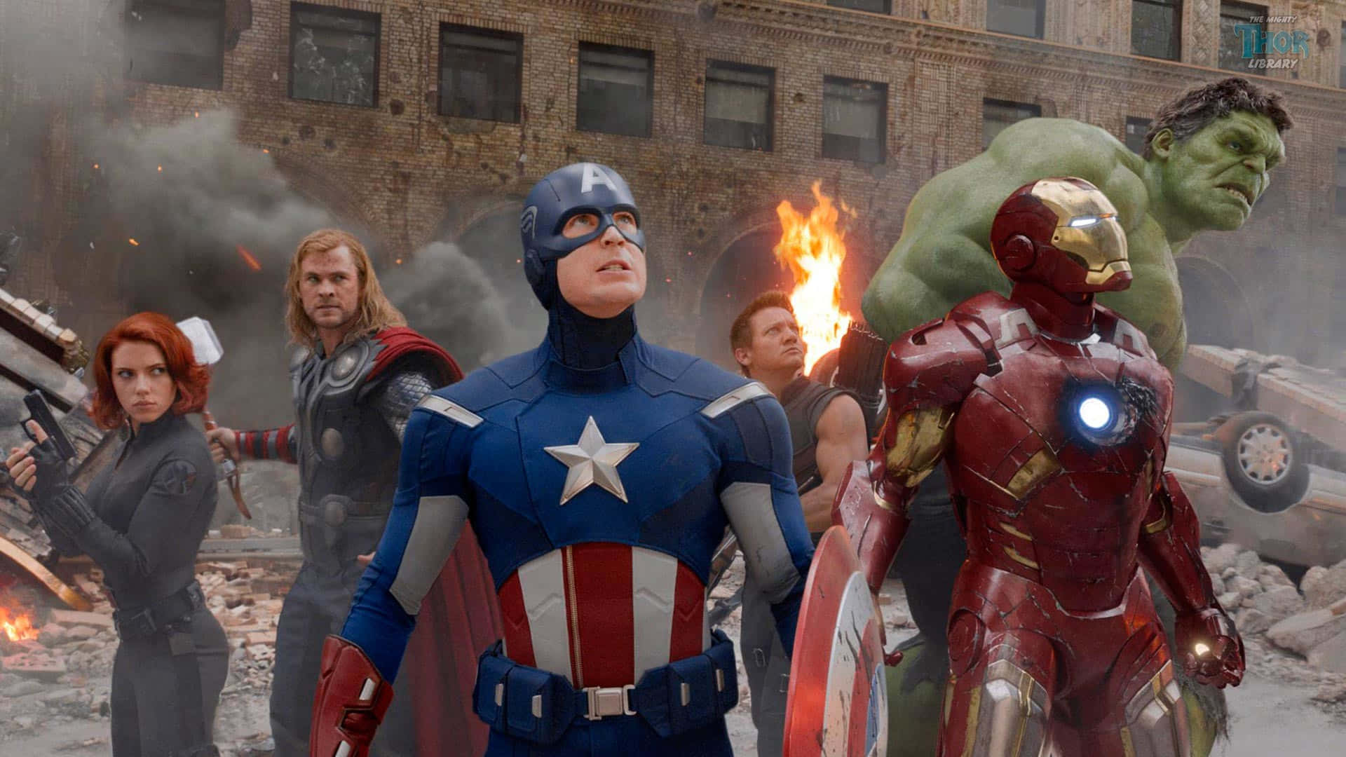 Avengers Movie 桌布 壁紙 — 超級英雄們在煙霧瀰漫的城市戰場上，背後是燃燒的瓦礫和搖搖欲墜的建築物，他們挑釁地站立著。