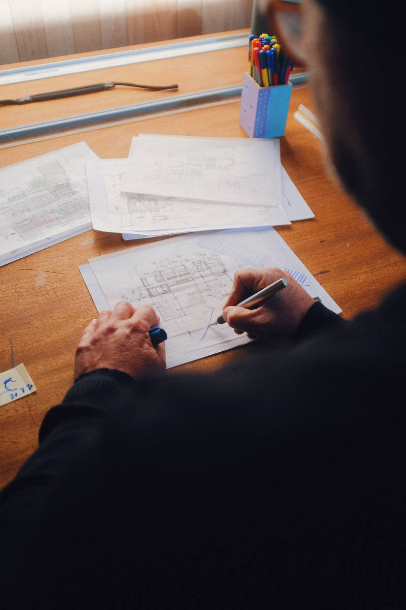 job 桌布 壁紙 — 越過肩膀的視角，一位建築師正在木桌上用彩色筆草繪藍圖。