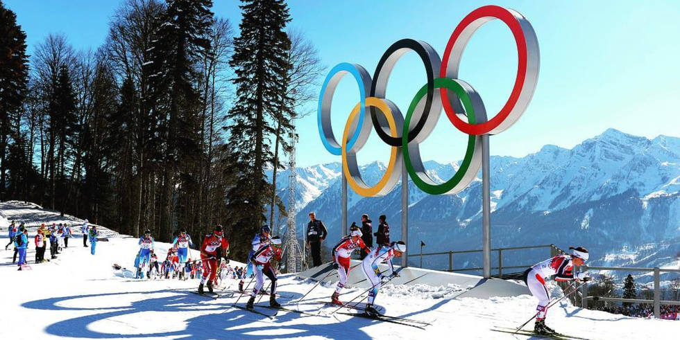 Winter Olympics 桌布 壁紙 — 越野滑雪運動員在晴朗藍天下，以積雪山脈為背景，經過巨大的奧運五環。