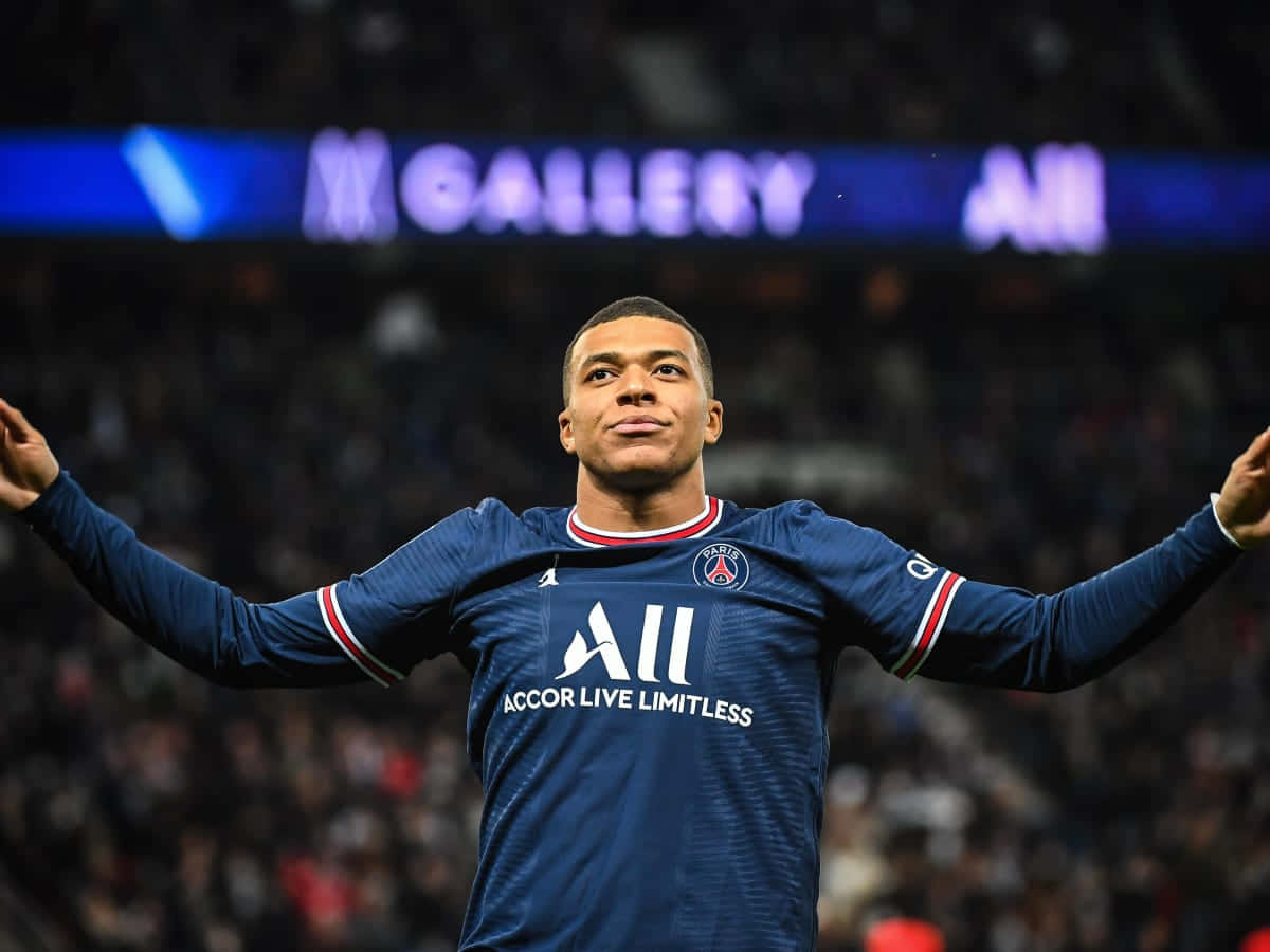 Mbappe 桌布 壁紙 — 足球員基利安·姆巴佩在球場燈光下身穿藍色PSG球衣，張開雙臂勝利慶祝。