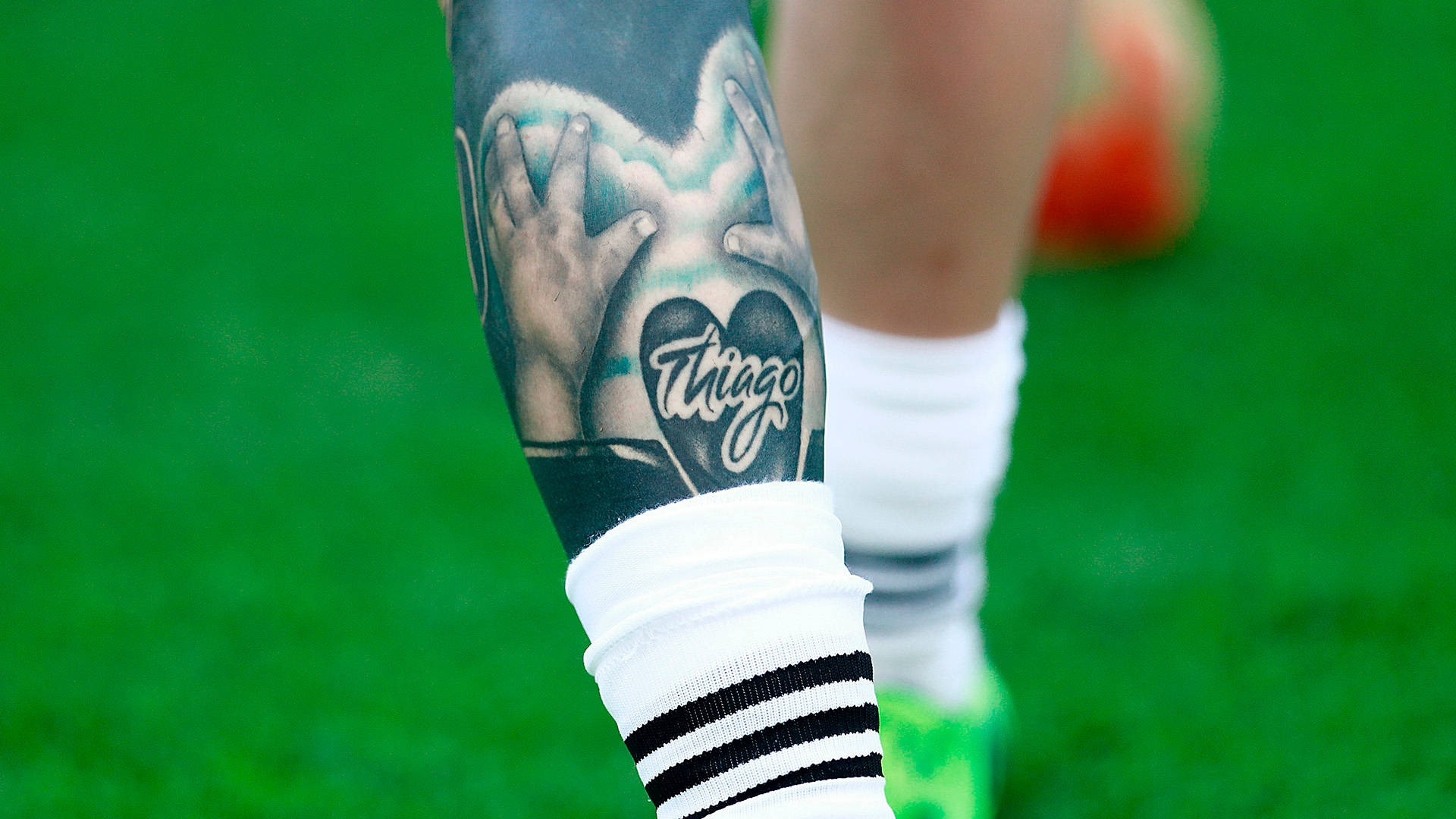 Tattoo 桌布 壁紙 — 足球員有刺青的小腿特寫，雙手形成心形，內有名字 'Trigo'，在充滿活力的綠色球場上。