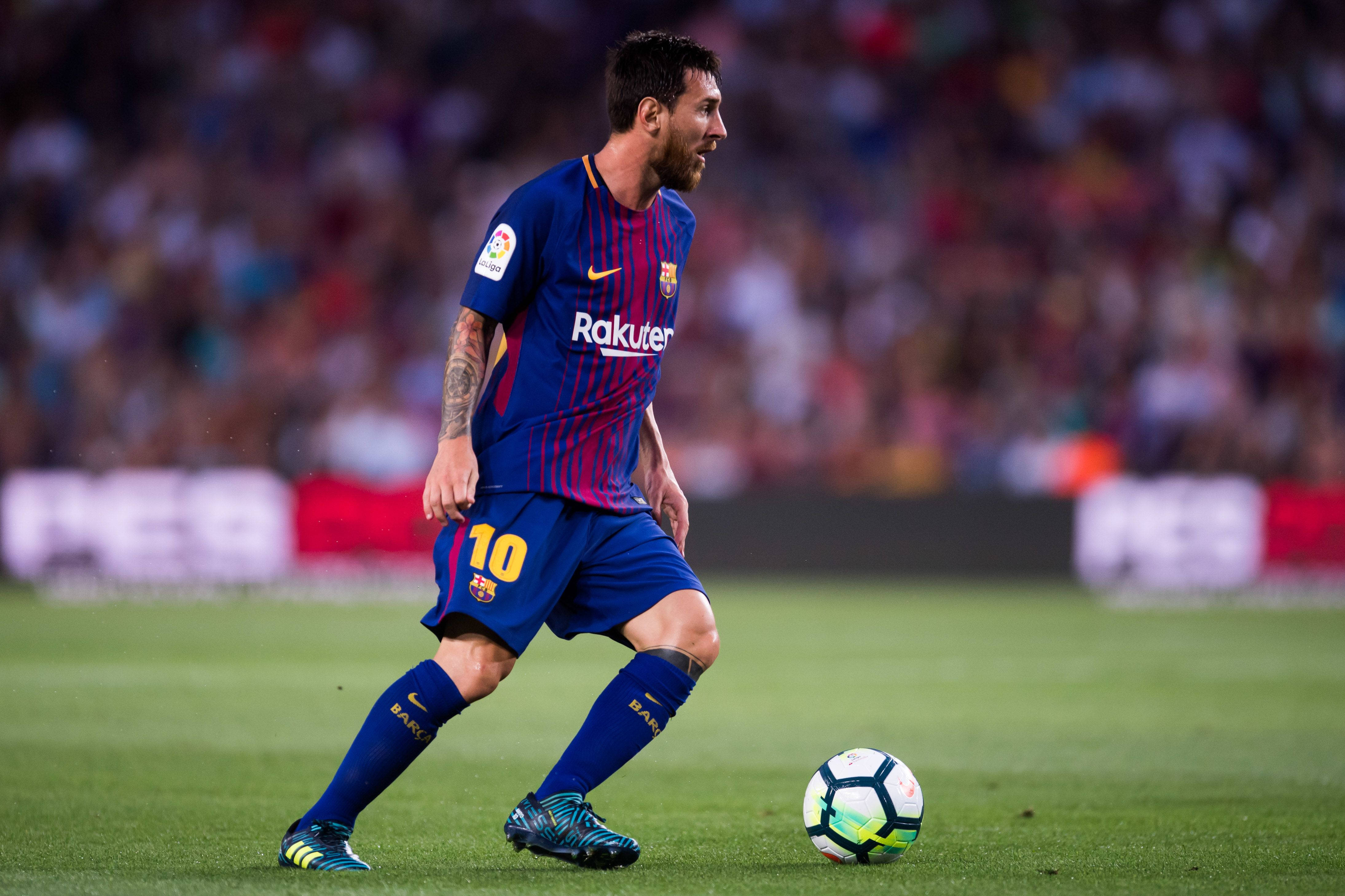 Messi 4K Ultra HD 桌布 壁紙 — 足球員梅西在體育場燈光下，於充滿活力的綠色球場上盤球，背景有模糊的觀眾。