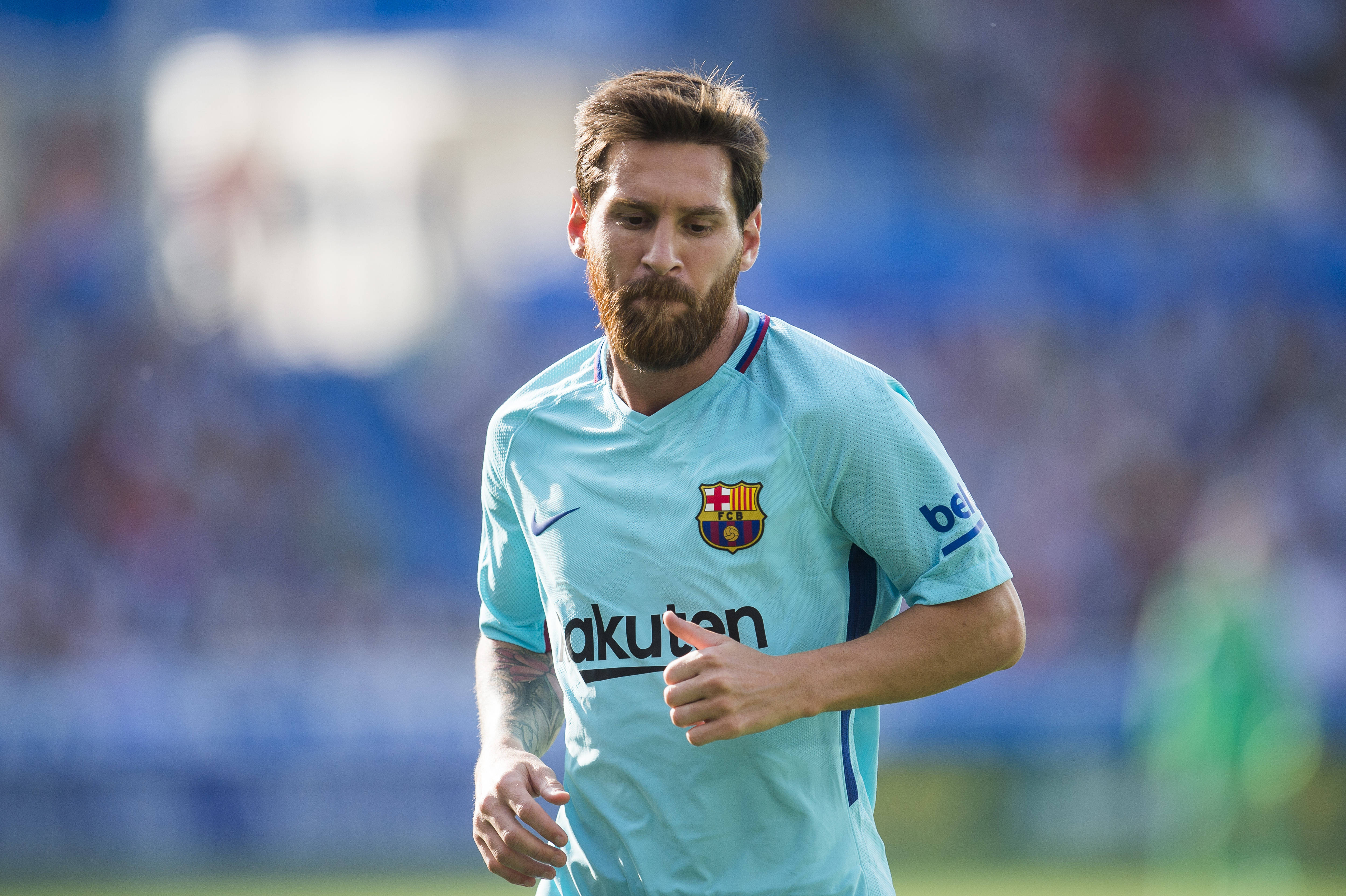 Messi 4K Ultra HD 桌布 壁紙 — 足球員梅西身穿淺藍色巴塞隆納球衣，在陽光明媚的球場上奔跑，身後是模糊的球場看台。
