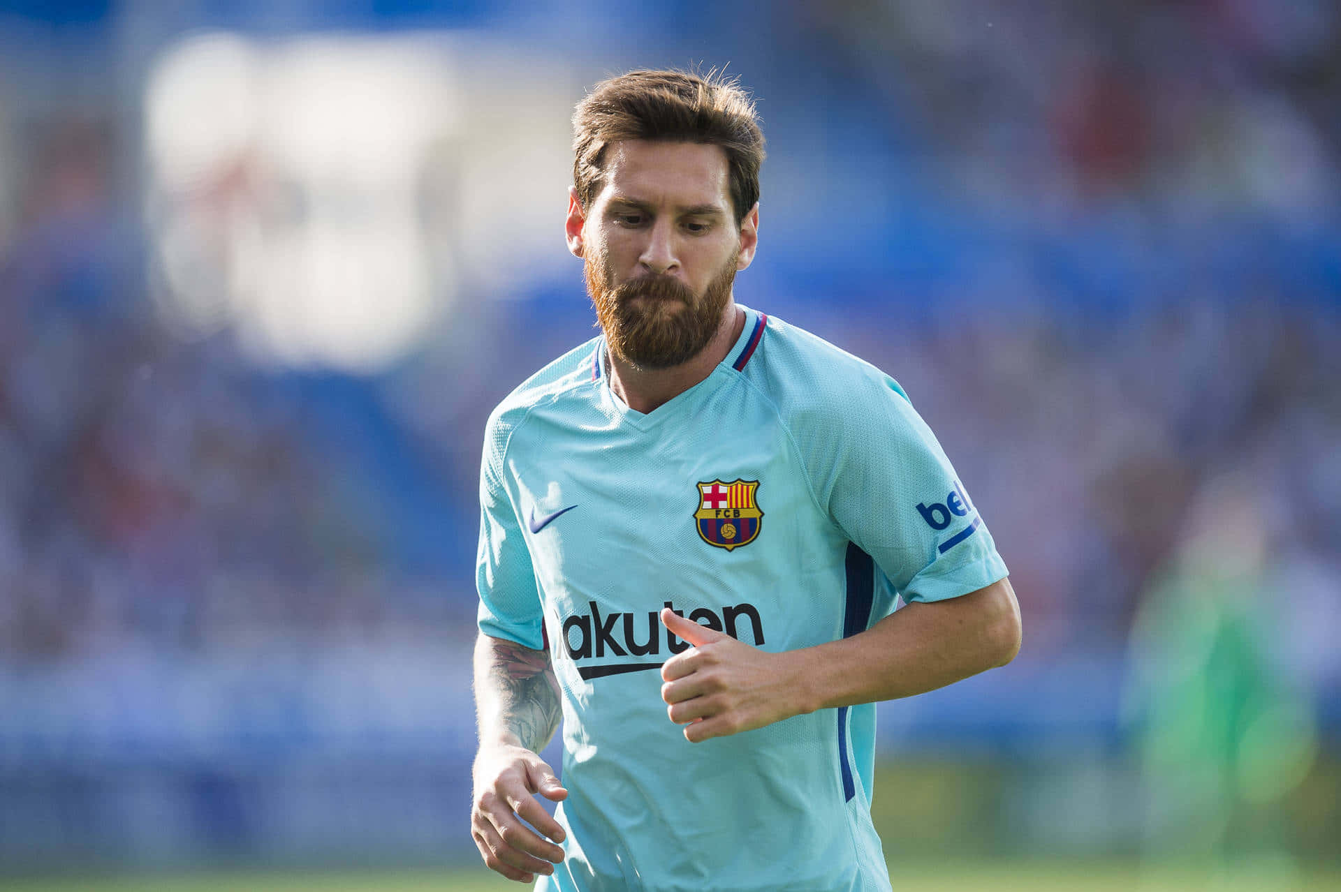 Messi Cool 桌布 壁紙 — 足球員梅西身穿淺藍色巴塞隆納球衣，在陽光明媚的球場上奔跑，背後是模糊的球場看台。