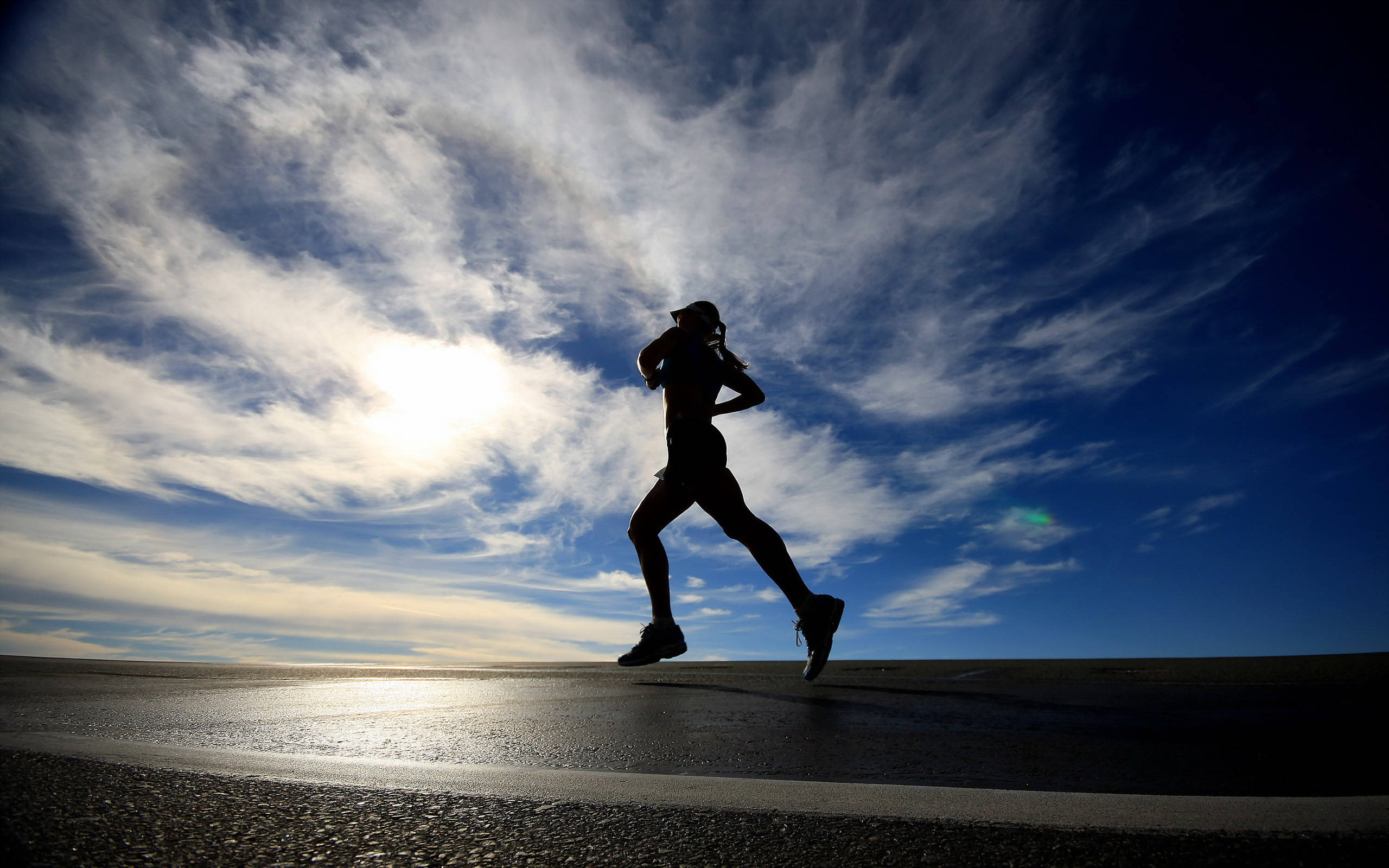 Athletic 桌布 壁紙 — 跑者的剪影沿著濕漉漉的道路大步前行，天空戲劇性，陽光透過縷縷雲層閃耀。