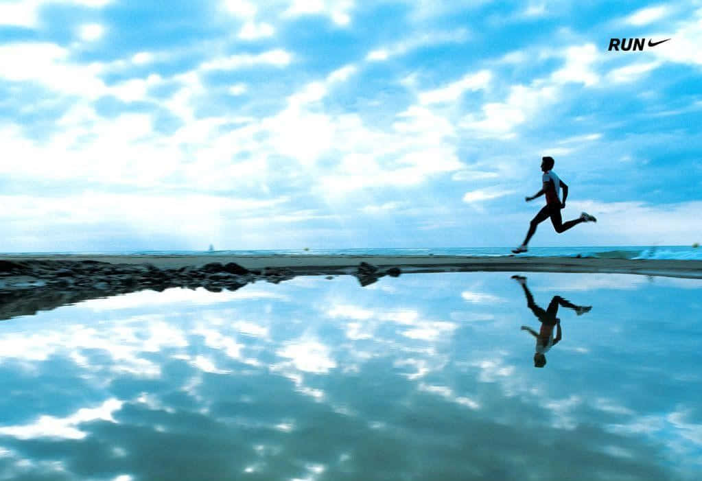 Run 桌布 壁紙 — 跑者的剪影躍過反射著明亮多雲天空的海灘水坑。