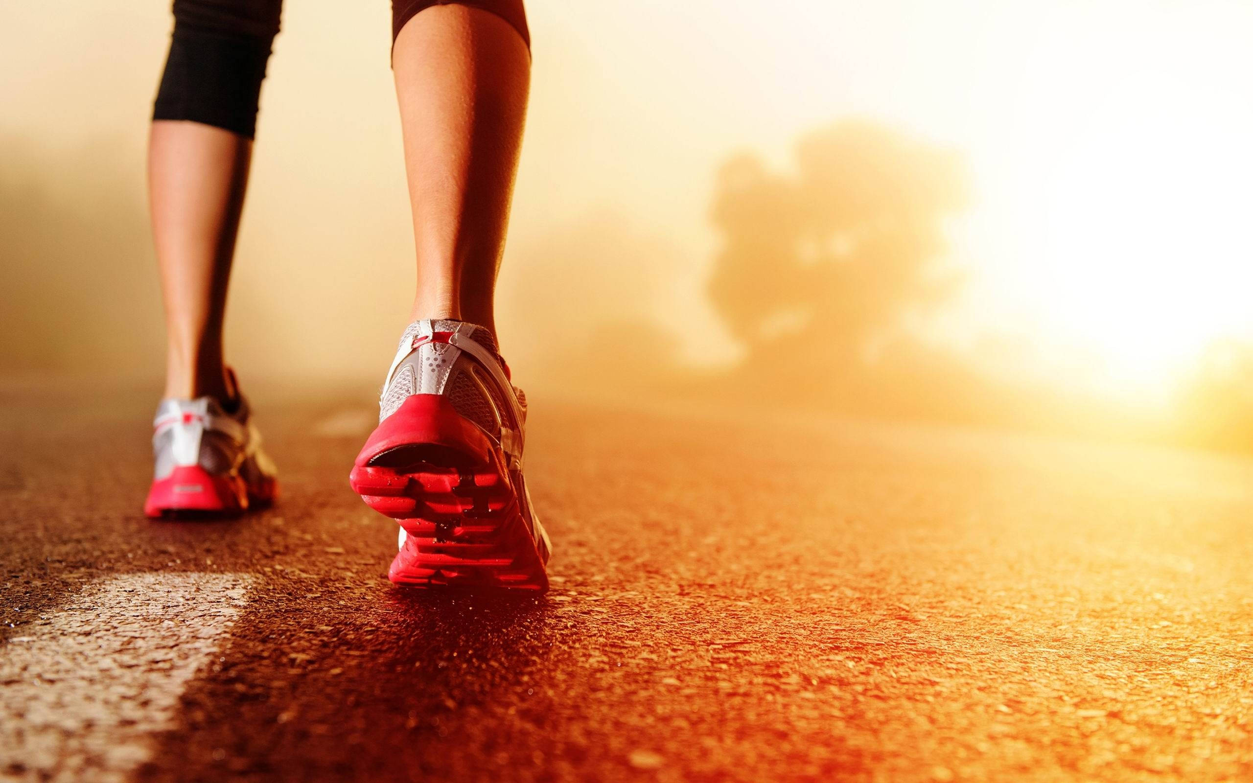 Exercise 桌布 壁紙 — 跑者穿著紅色運動鞋的腳部特寫，在陽光照耀的道路上向前邁步，帶有溫暖的金色光芒。