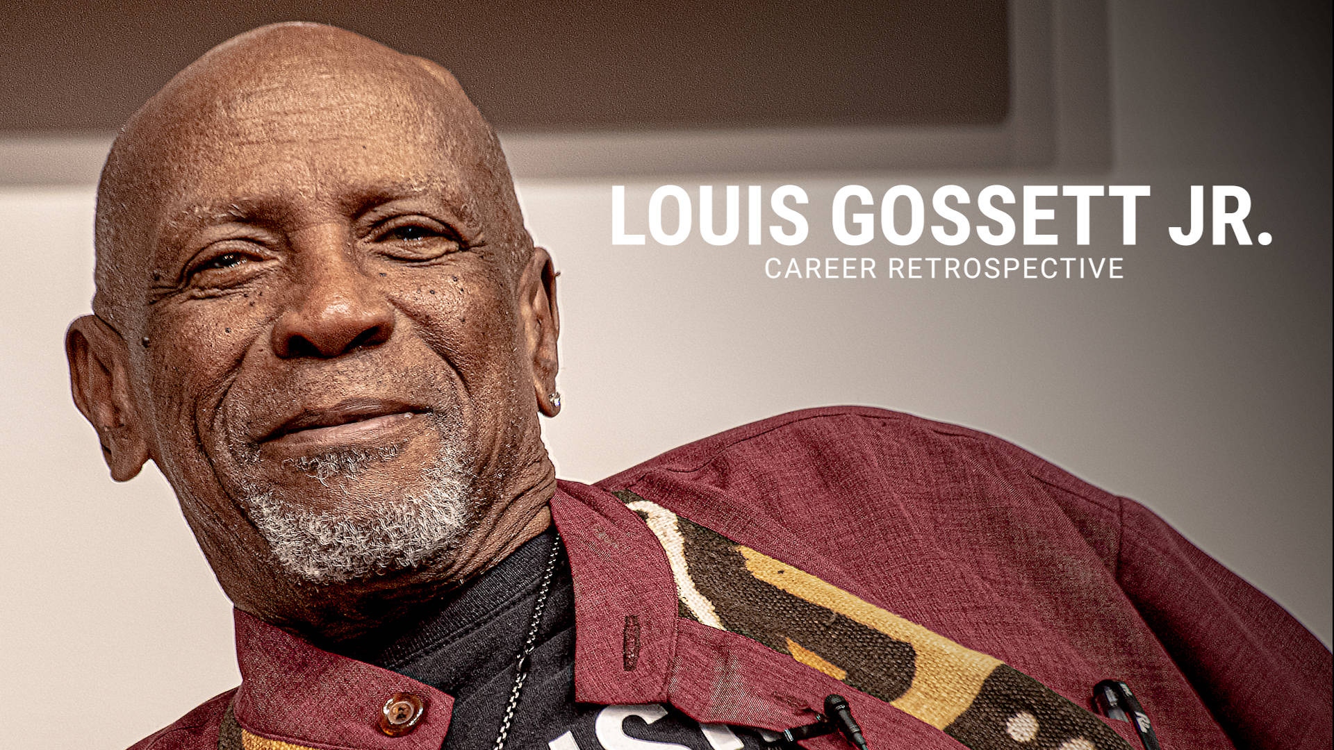Celebrity 桌布 壁紙 — 路易斯·高塞特（Louis Gossett Jr.）身穿栗色圖案外套，在中性背景前溫暖微笑的特寫肖像。