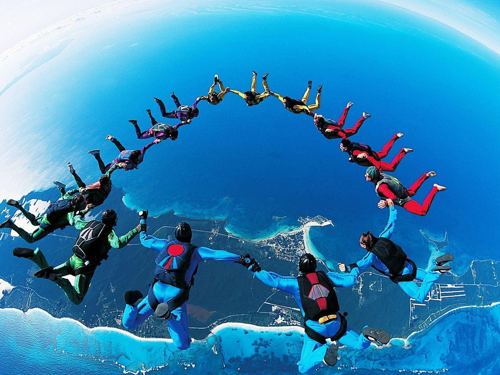 Teamwork 桌布 壁紙 — 跳傘者在下方彎曲的藍色地球上形成一個充滿活力的人類圓圈。