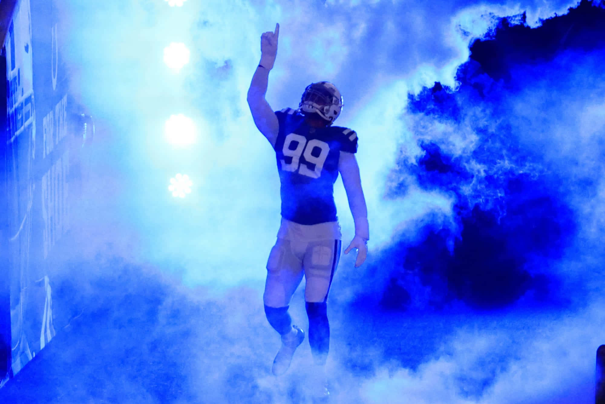 Football Players 桌布 壁紙 — 身穿99號球衣的足球運動員在明亮的體育場燈光下穿過藍色煙霧入場。