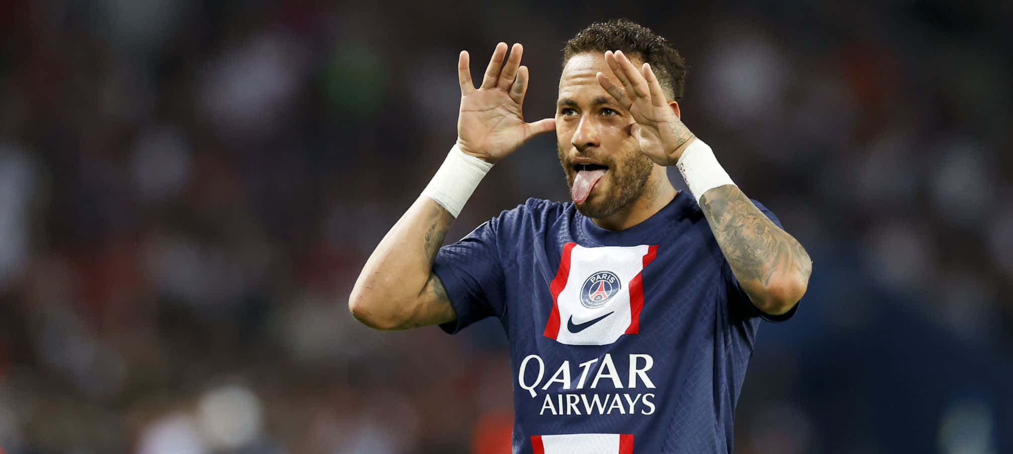 内马尔 桌布 壁紙 — 身穿PSG球衣的足球員內馬爾（Neymar Jr）在球場燈光下頑皮地伸出舌頭並向球迷揮手。