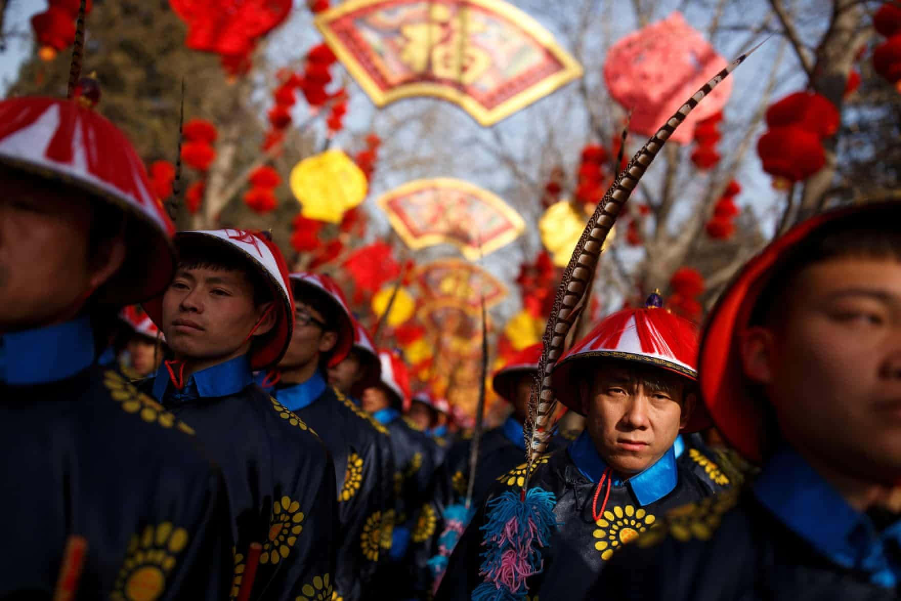 春節 桌布 壁紙 — 身穿傳統紅藍色儀式制服、戴著羽毛帽的男子，在鮮紅的燈籠和節日橫幅下遊行。
