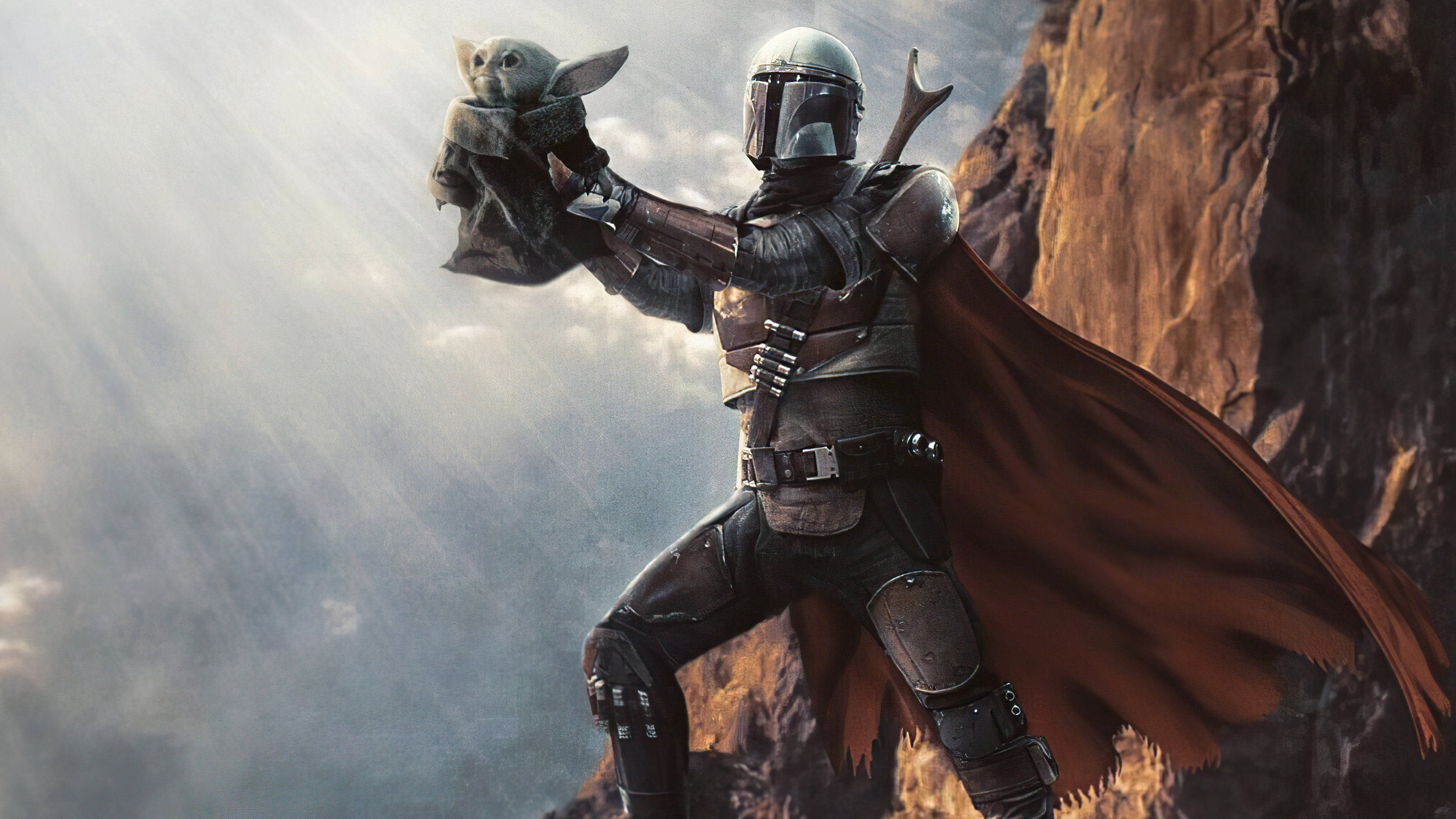 Mandalorian And Baby Yoda 桌布 壁紙 — 身穿全套盔甲的曼達洛人在戲劇性的懸崖背景下抱著古古，陽光穿過雲層照射下來。