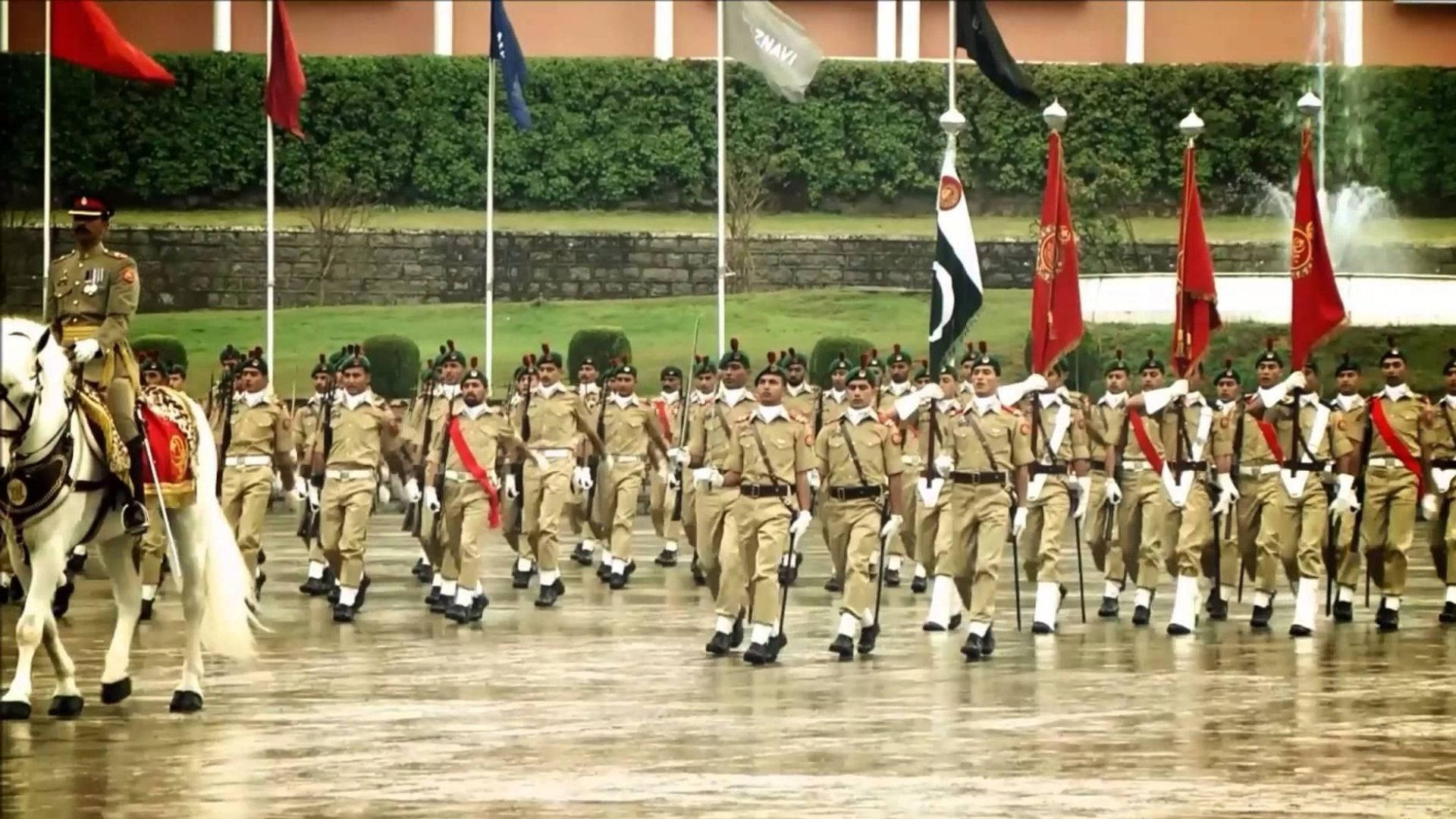 Pakistan 桌布 壁紙 — 身穿制服的士兵在陰天潮濕的閱兵場上精確地列隊行進，背景中旗幟飄揚。