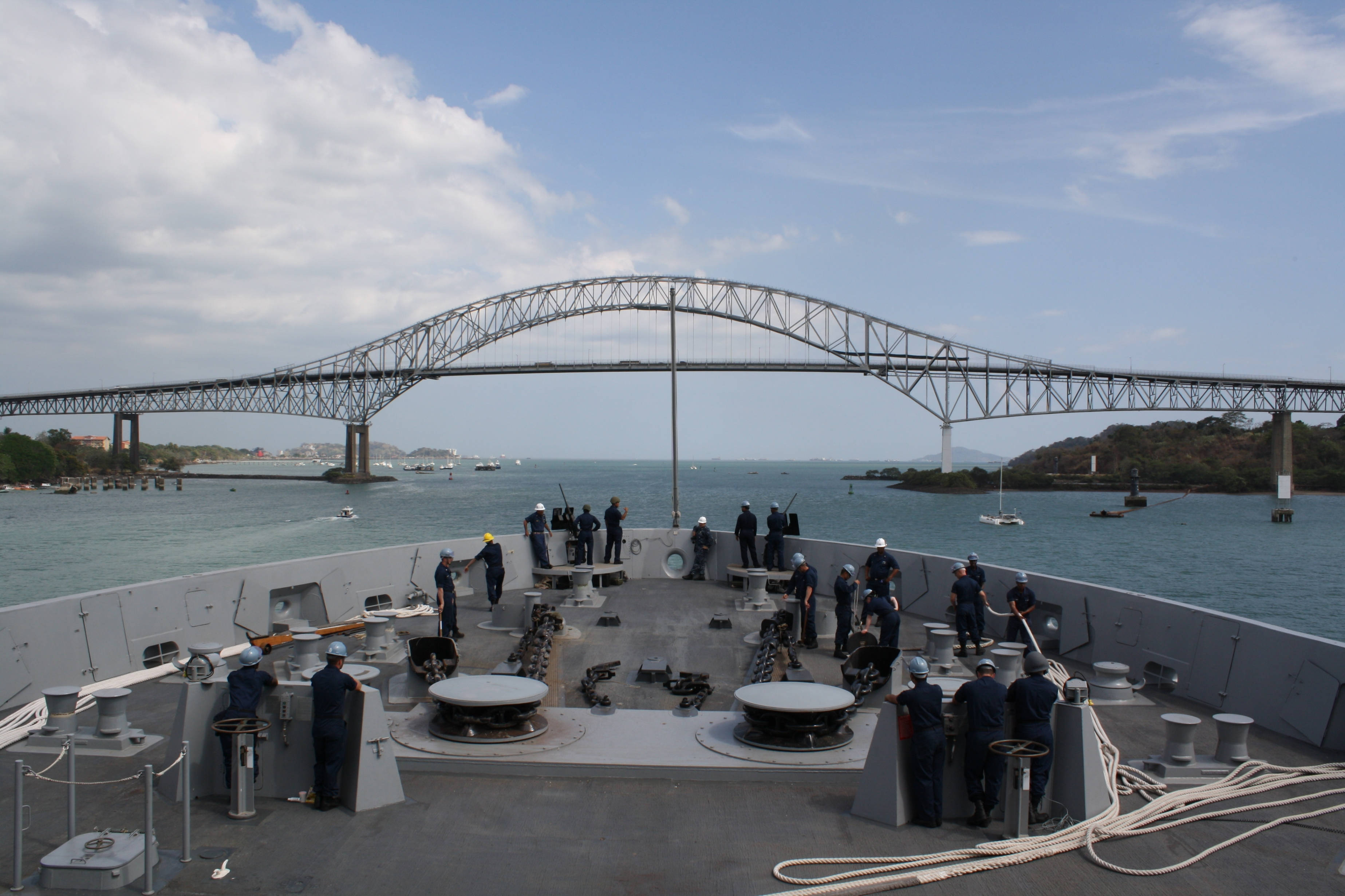Panama 桌布 壁紙 — 身穿制服的海軍船員站在軍艦甲板上，甲板上有大型火炮，藍天之下，身後一座鋼拱橋橫跨海洋。