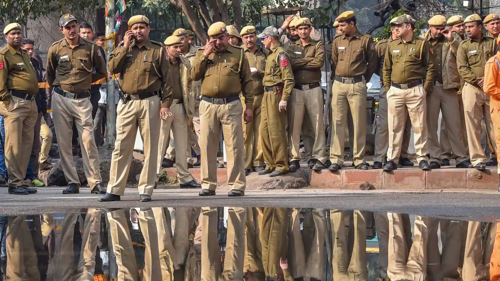 Indian 桌布 壁紙 — 身穿制服的警察在濕漉漉的街道上排成一列，他們的倒影完美地映照在下面的水坑中。