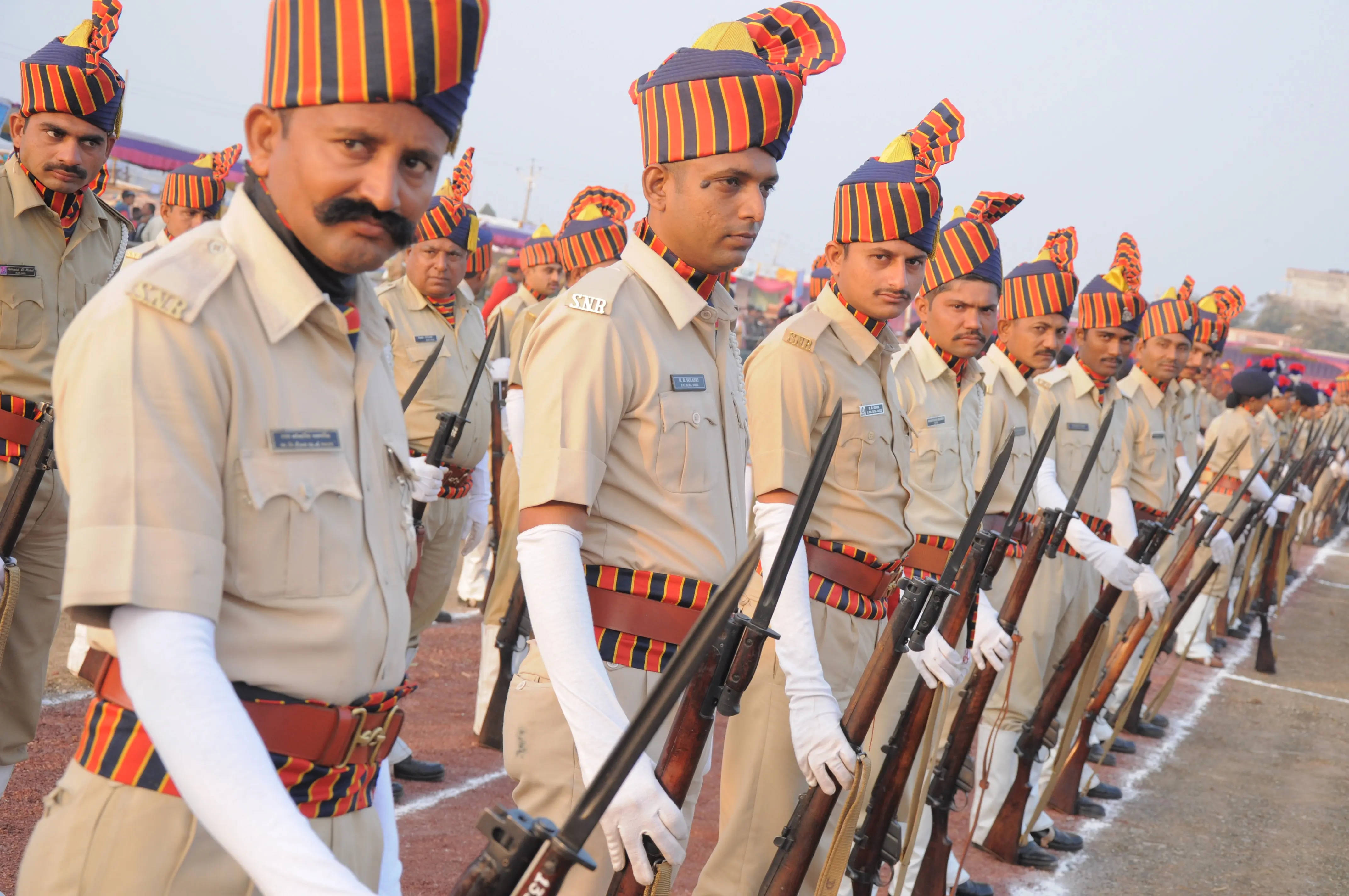 Indian 桌布 壁紙 — 身穿卡其色制服和彩色條紋頭巾的制服士兵在儀式遊行中精確地排列成隊形，手持步槍立正。