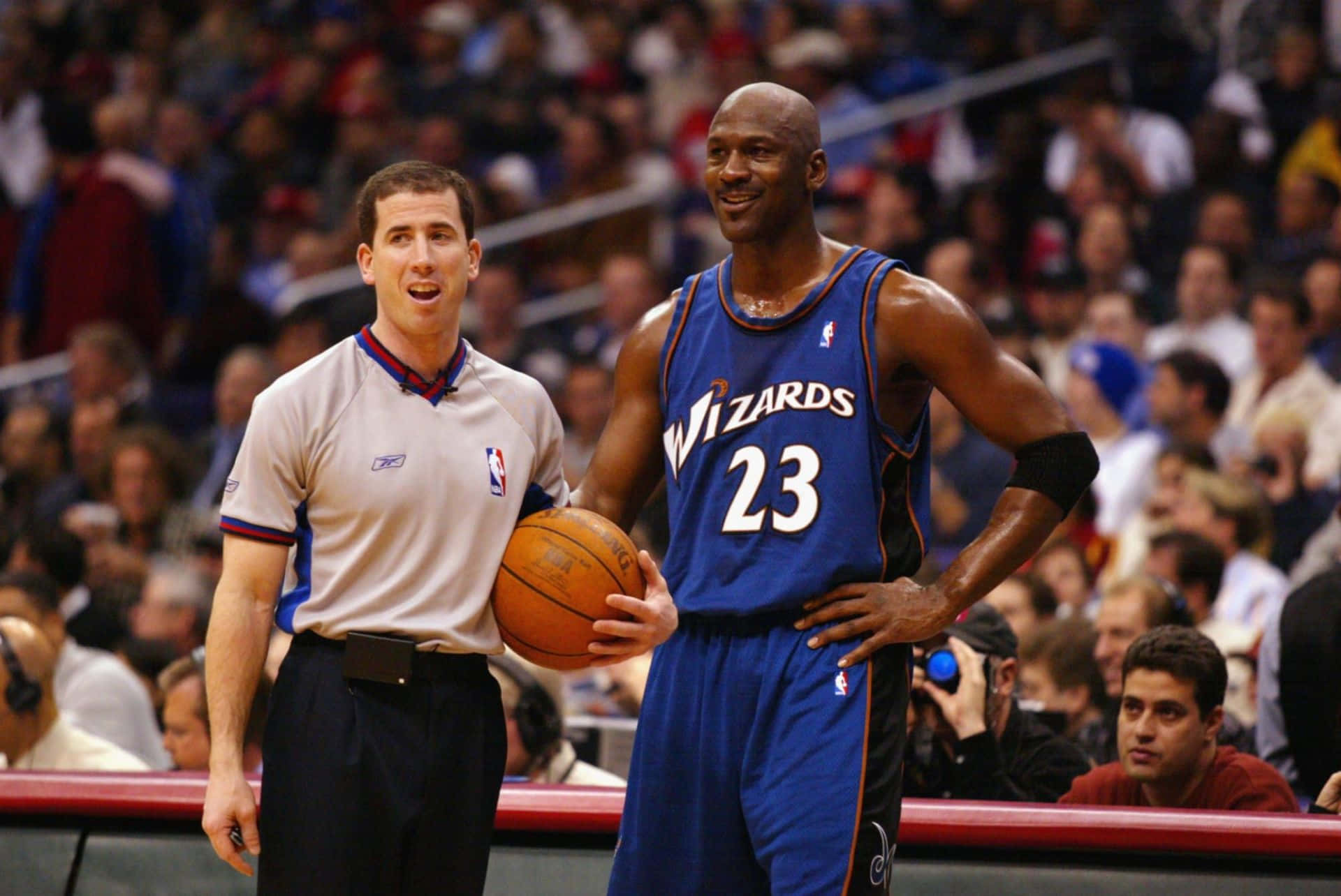 身穿巫師隊球衣的麥可喬丹在NBA比賽中，拿著籃球站在裁判旁邊。 — Michael B Jordan 壁紙
