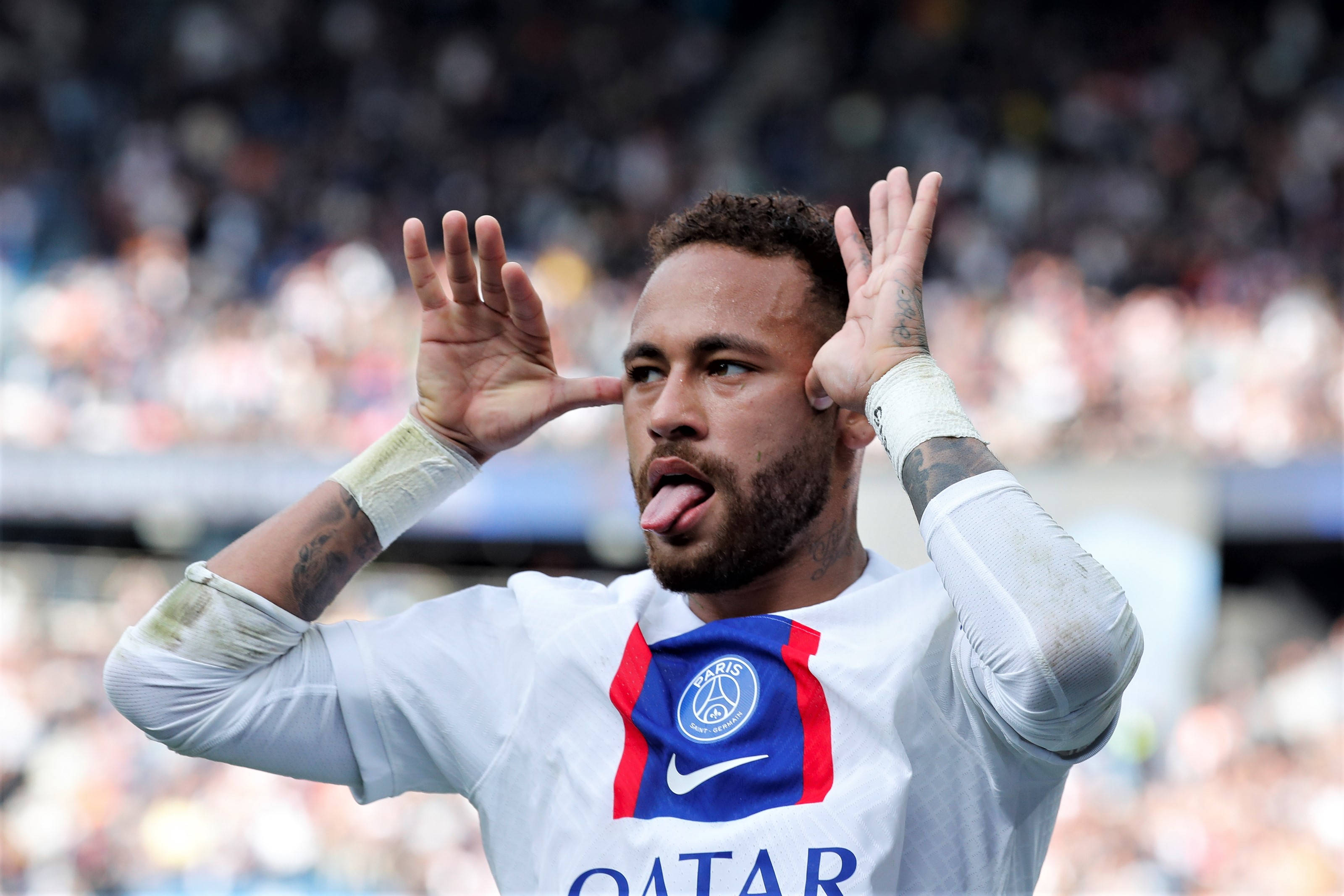 足球 桌布 壁紙 — 身穿巴黎聖日耳曼球衣的足球員內馬爾（Neymar Jr）在體育場人群中頑皮地伸出舌頭並舉起雙手。